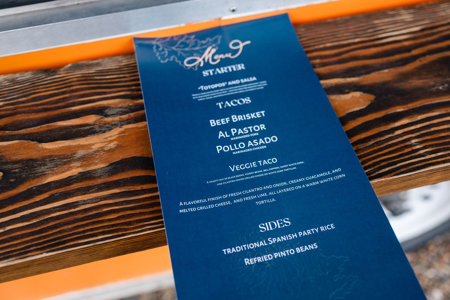 Navy blue wedding menu card with white text displayed on rustic wooden surface.