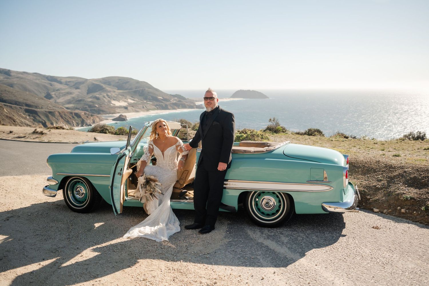 Vintage turquoise car parked along scenic coastal cliff during sunset.