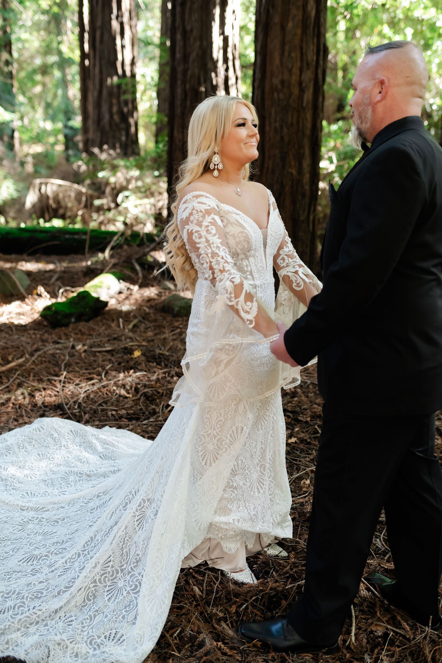 A romantic wedding moment captured in a redwood forest with flowing lace dress details.