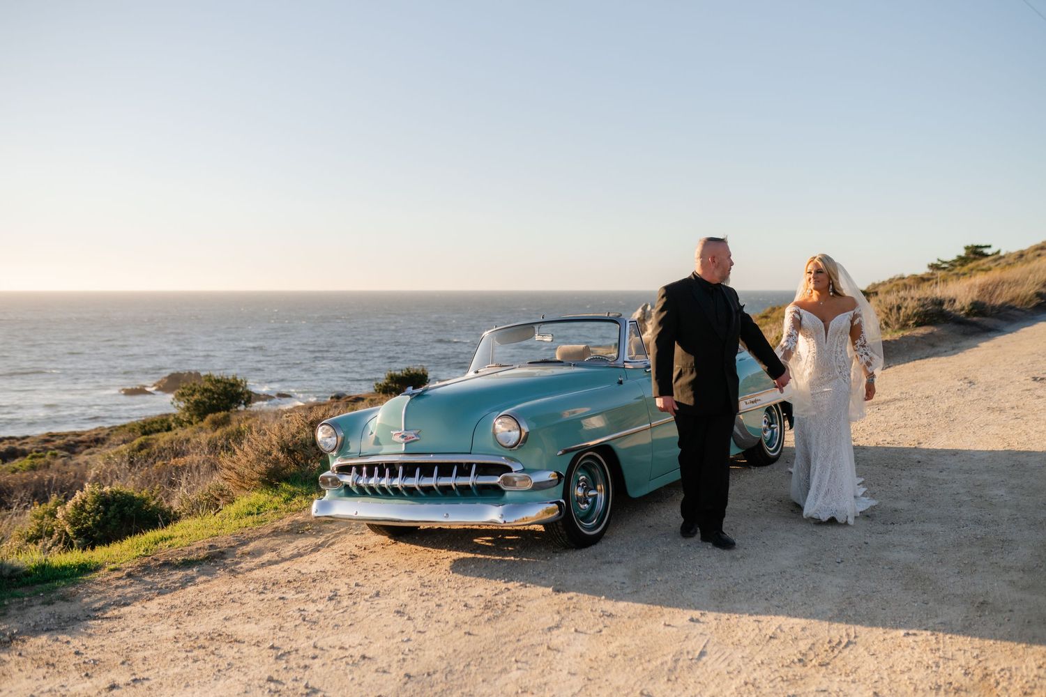 Classic turquoise convertible car parked along rugged coastline with ocean views.