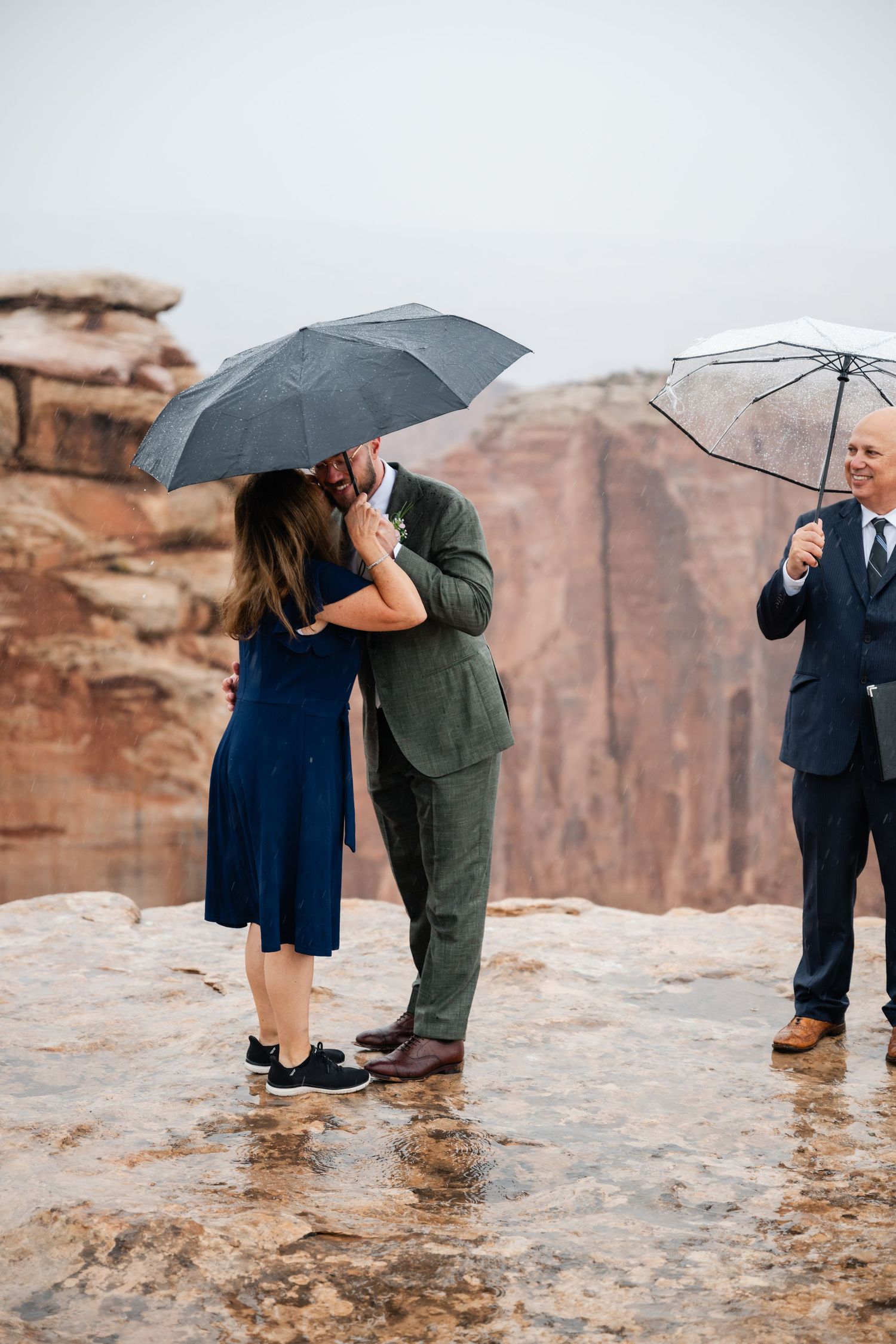 Wedding ceremony in the rain with umbrellas on dramatic cliffside overlook.