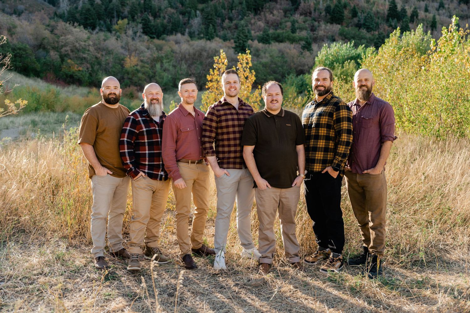 People wearing earth-toned clothing stand together for a group photo against a backdrop of autumn foliage.