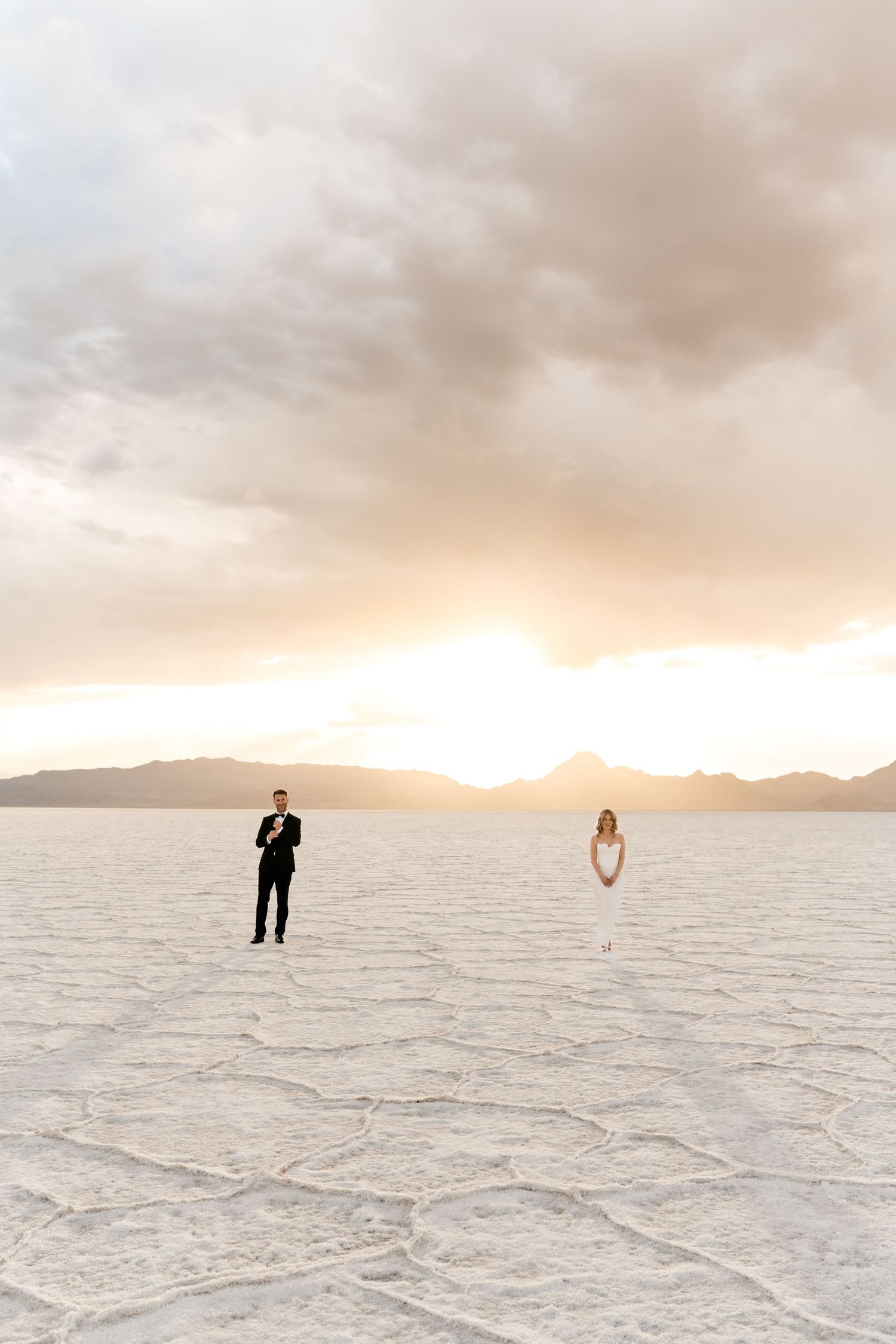 Salt Flats Elopement Photographer. A couple in formal attire stands far apart on the stark white salt flats during sunset.