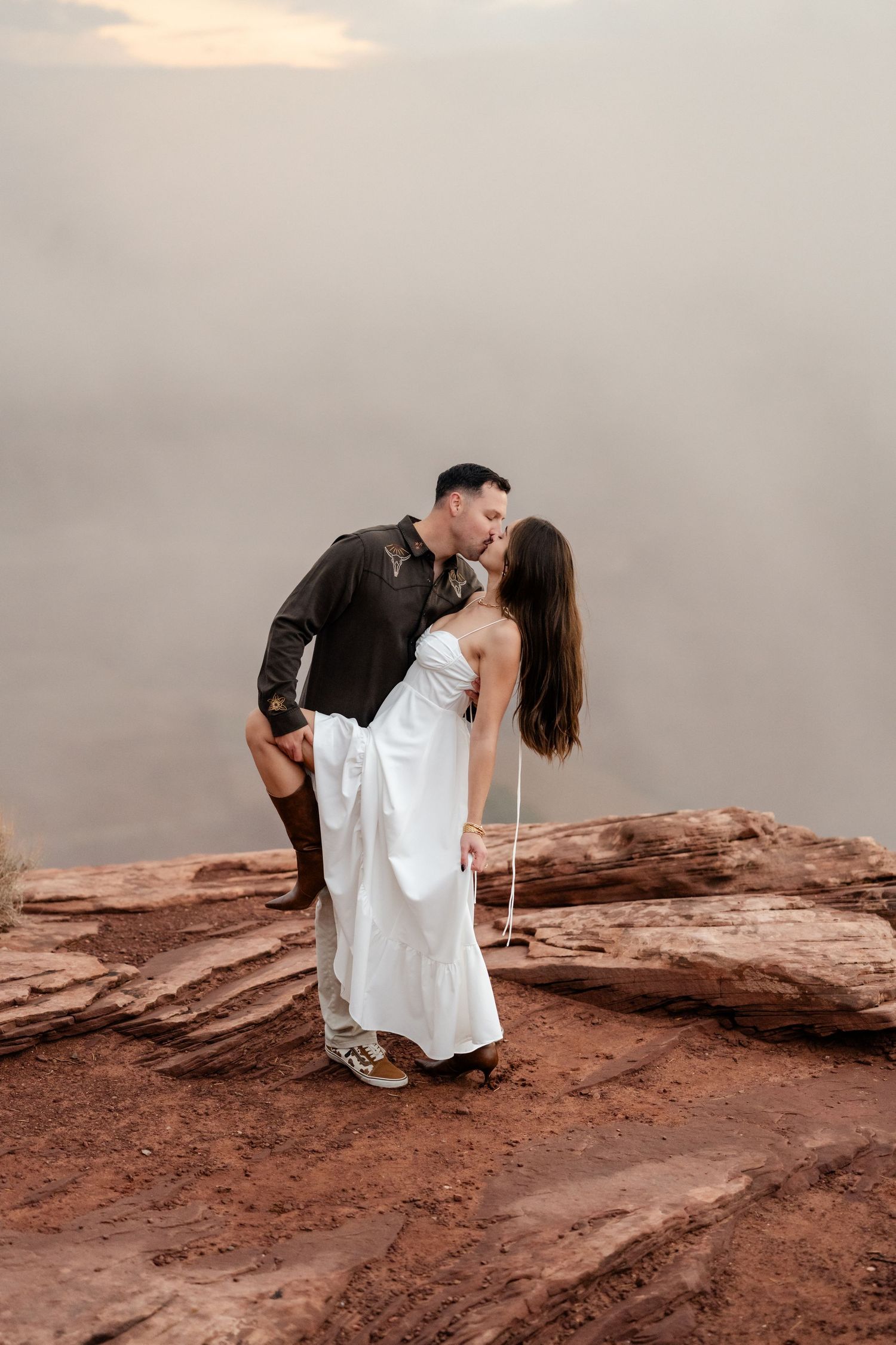 Romantic couple sharing intimate moments on red rock formations at sunset.
