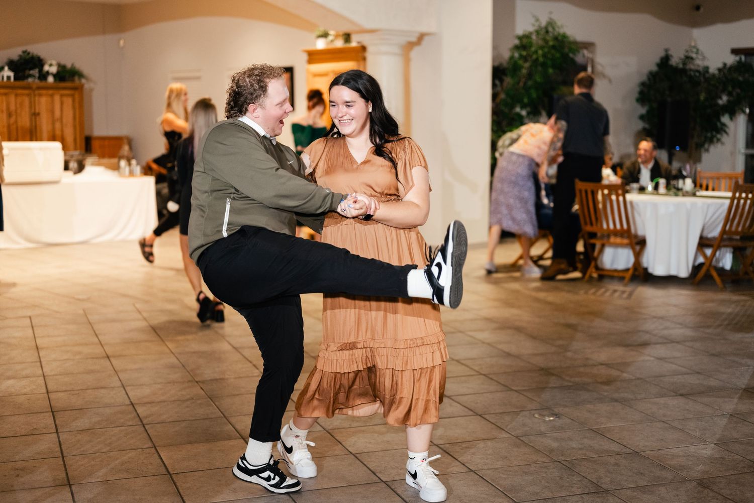 Two guests dance energetically together on the tiled dance floor at a wedding reception.