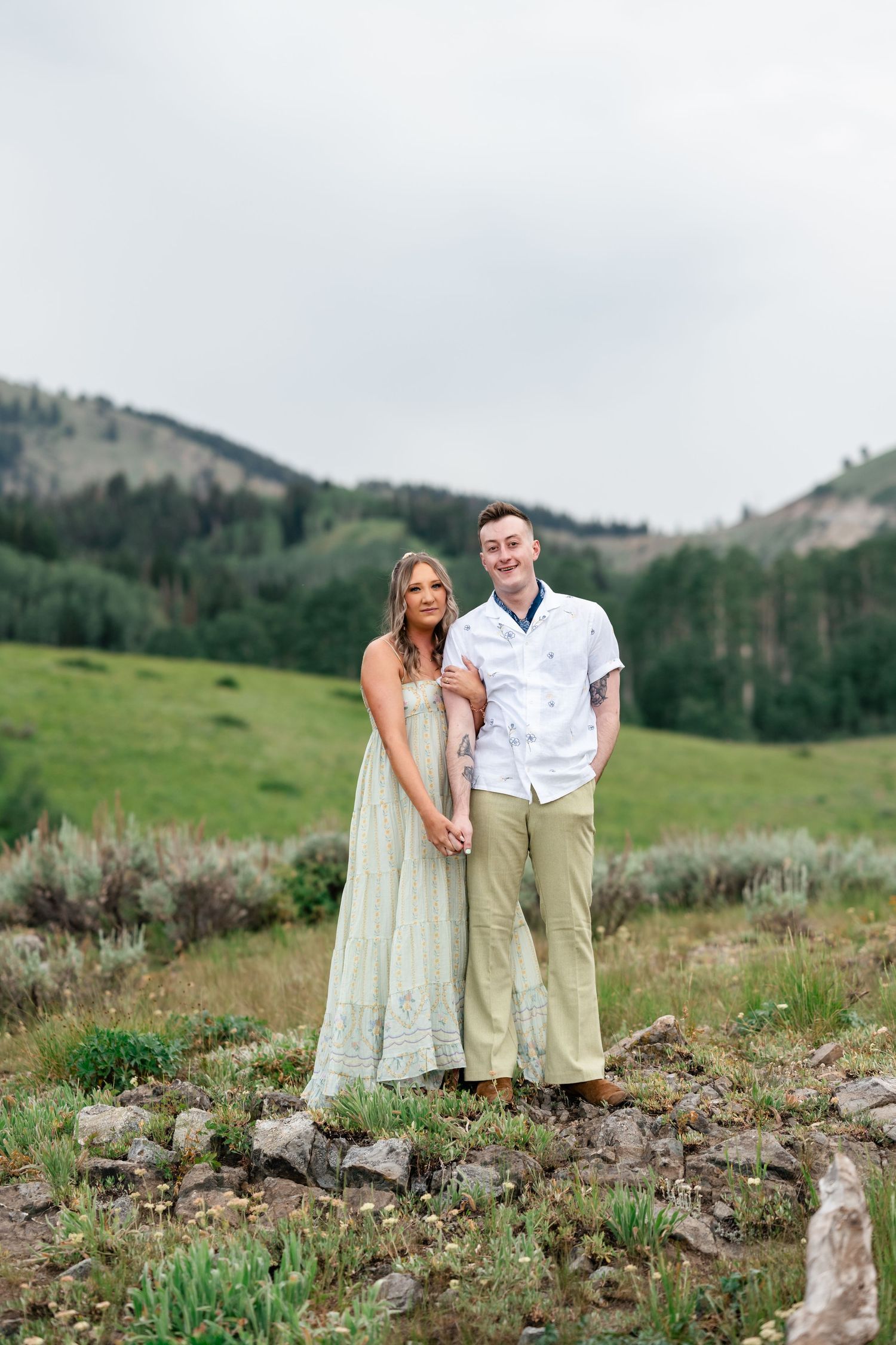 A romantic outdoor portrait of a couple standing together in a green mountain meadow on a cloudy day. Park City engagement photographer