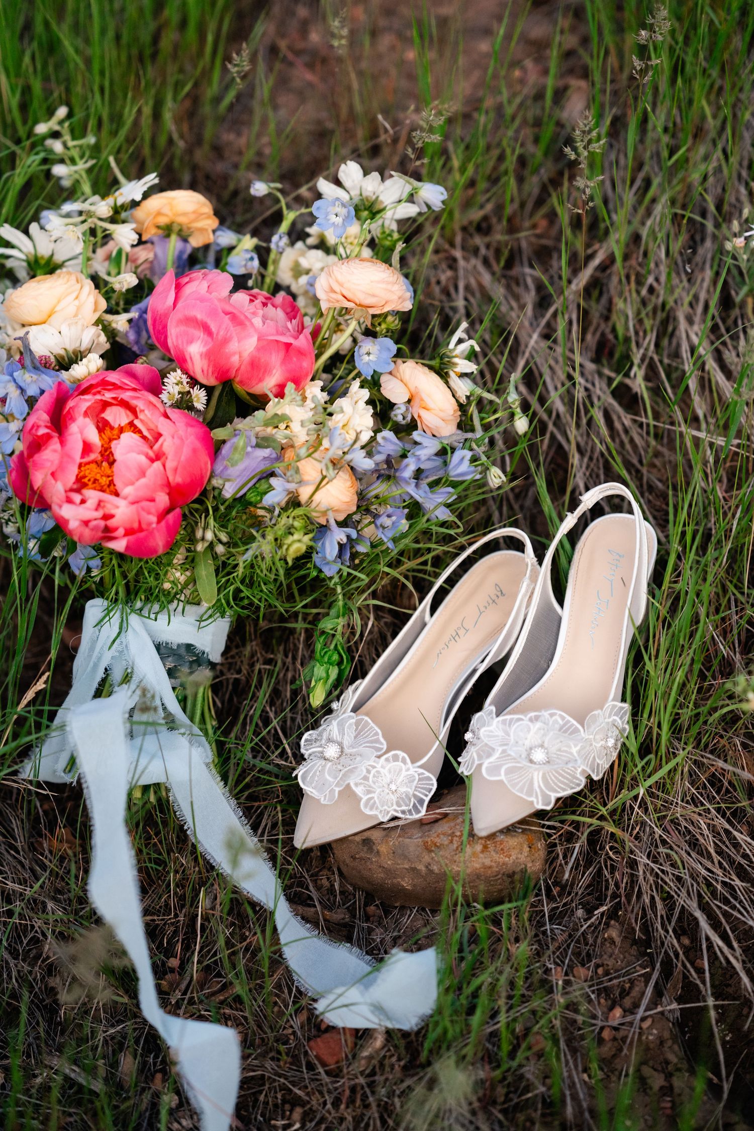 Wedding details showing delicate lace shoes next to pink peony and rose bouquet.
