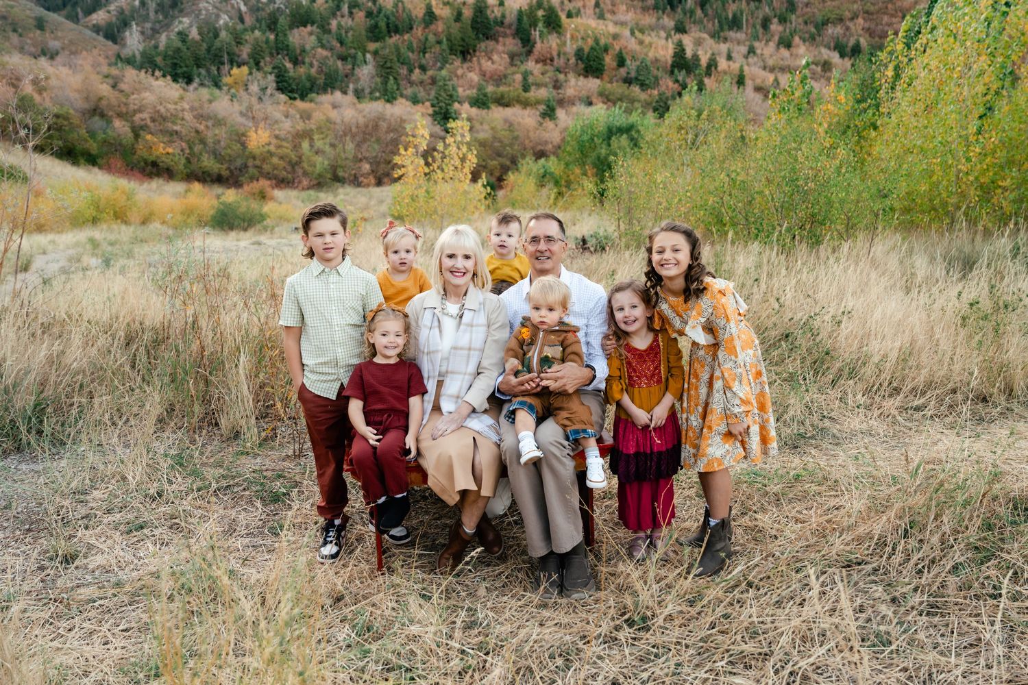 A group in coordinated fall outfits poses together in a natural outdoor setting with brown grass and greenery.