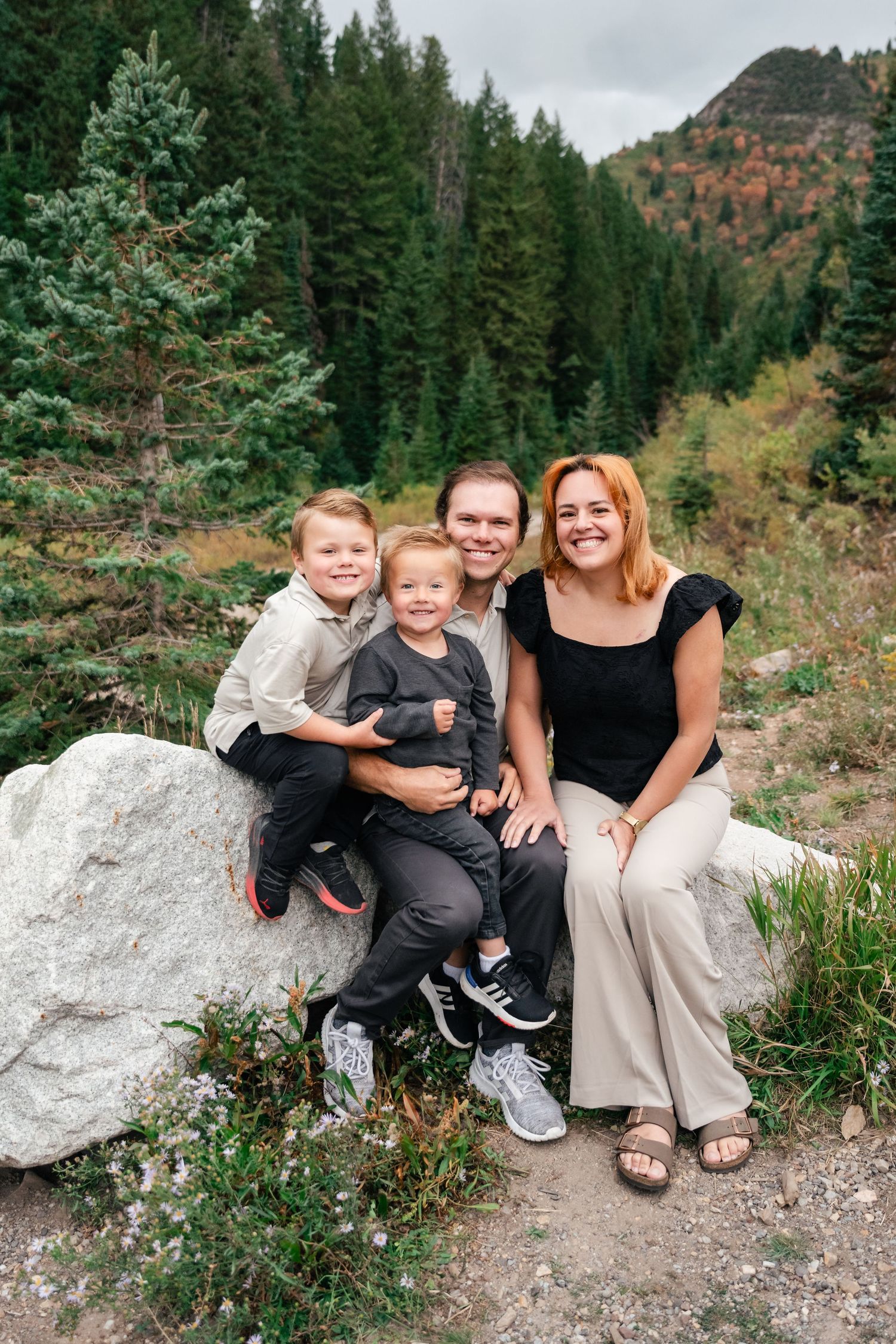 A group sits together on a white rock formation along a mountain trail surrounded by evergreen trees and vegetation.