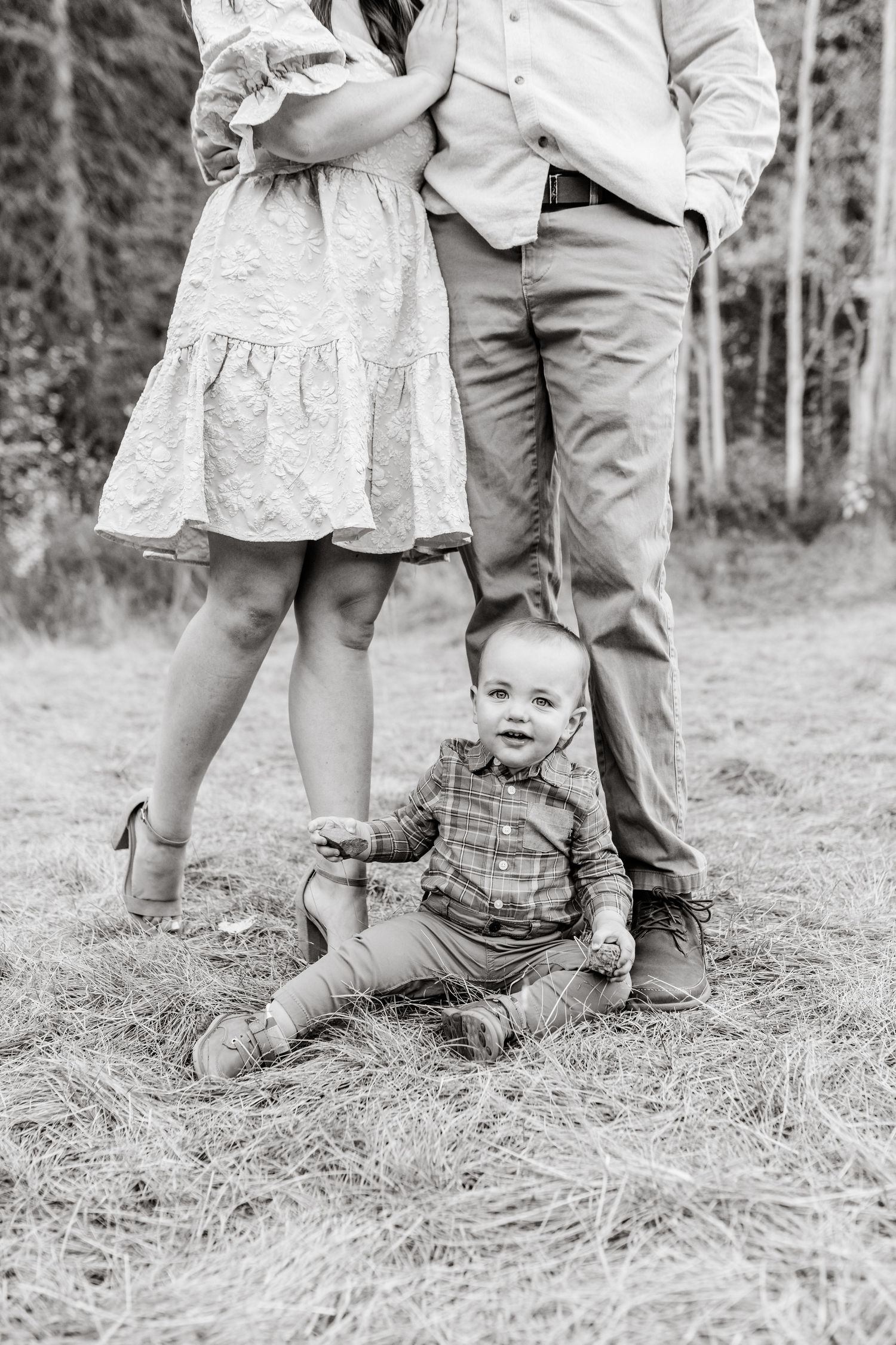 Black and white photo showing legs and feet of a family standing together in a grassy field.