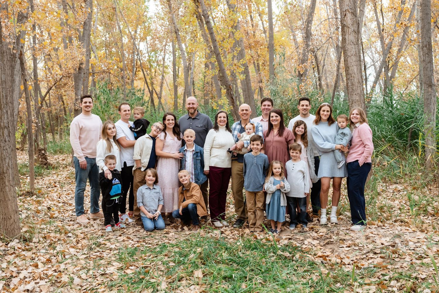A large group gathers for an autumn photo in a wooded area with fallen leaves and golden foliage.