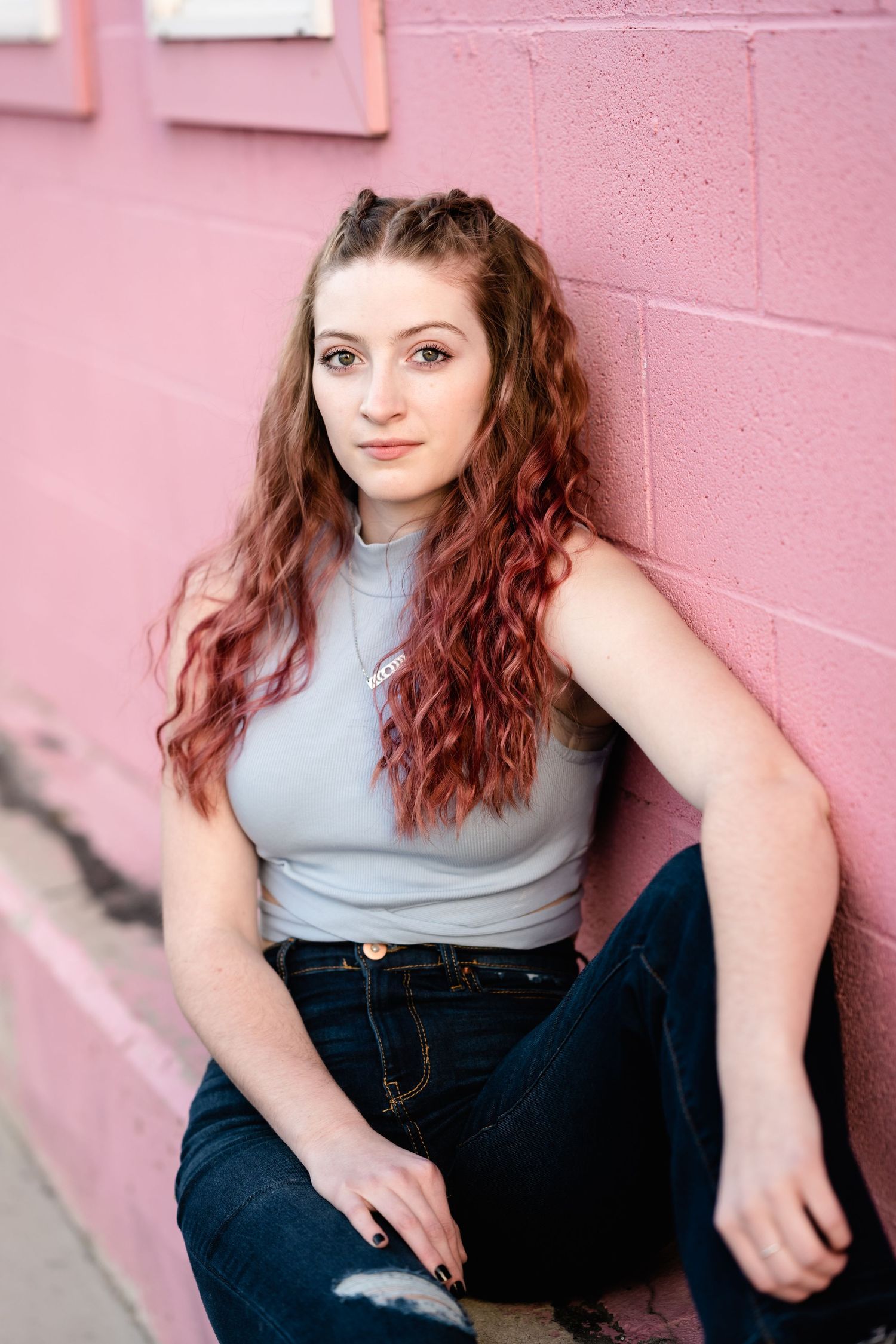 A series of portraits against a pink wall showing someone in a light blue top and dark jeans with curly auburn hair.