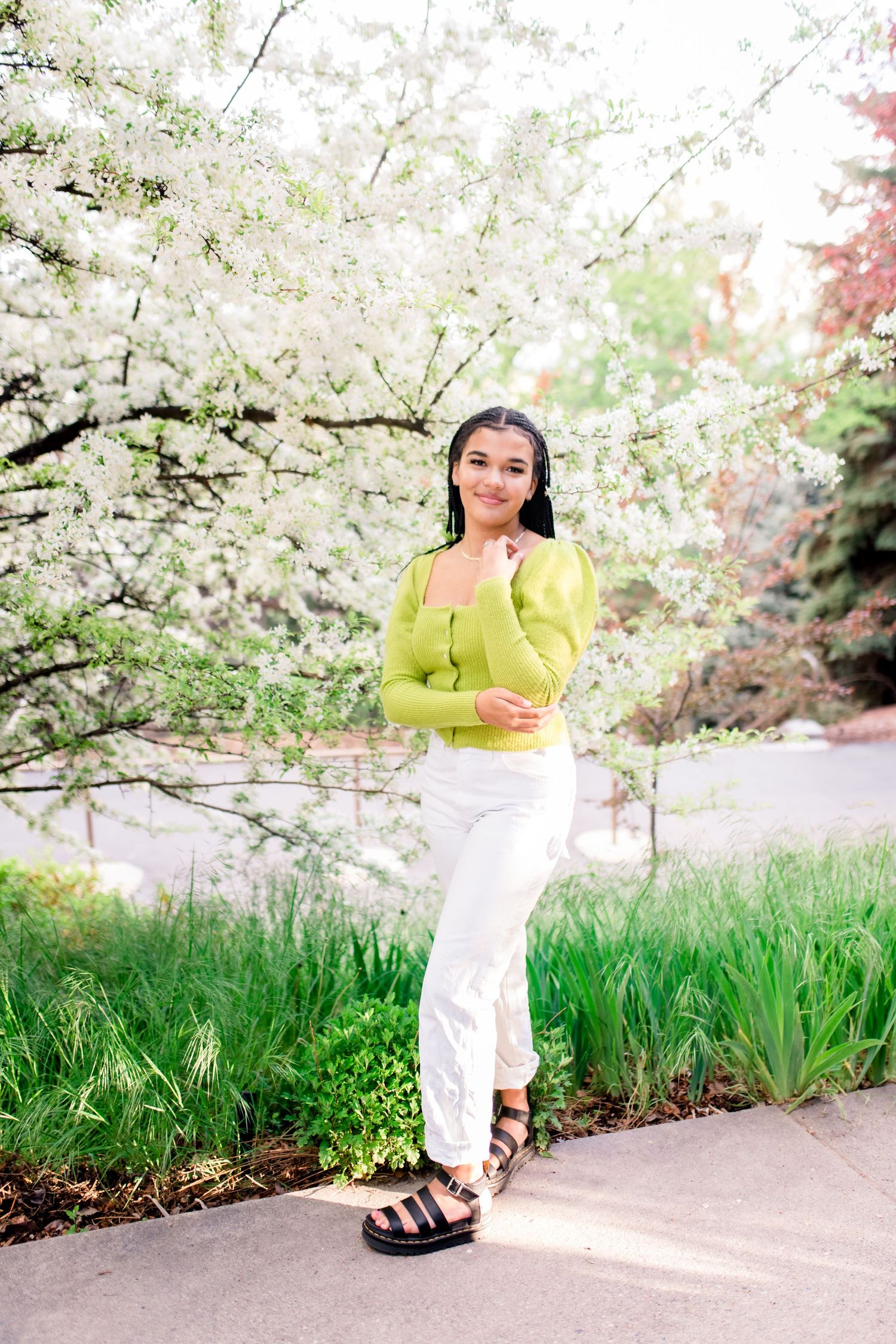 A person in a bright yellow top and white pants poses among blooming cherry blossom trees on a spring day.