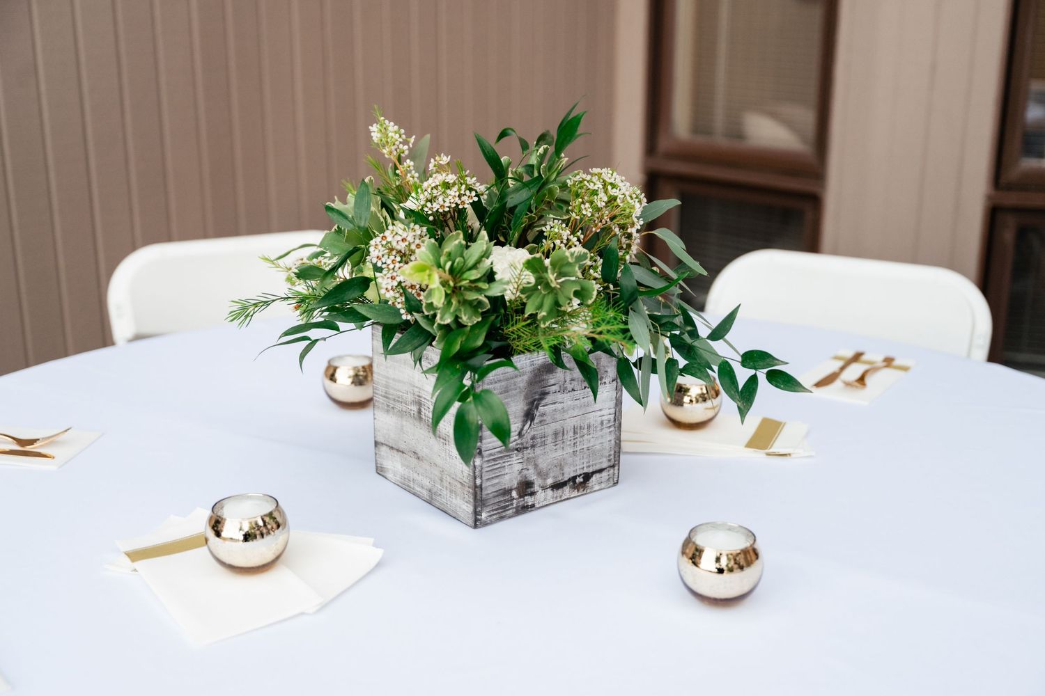 Elegant white floral centerpiece in a wooden box on a table with metallic decorative spheres.