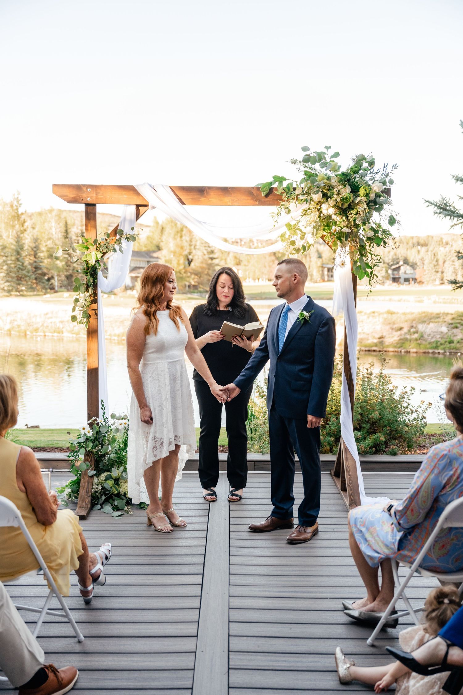 Intimate outdoor wedding ceremony on a wooden deck overlooking a pond.