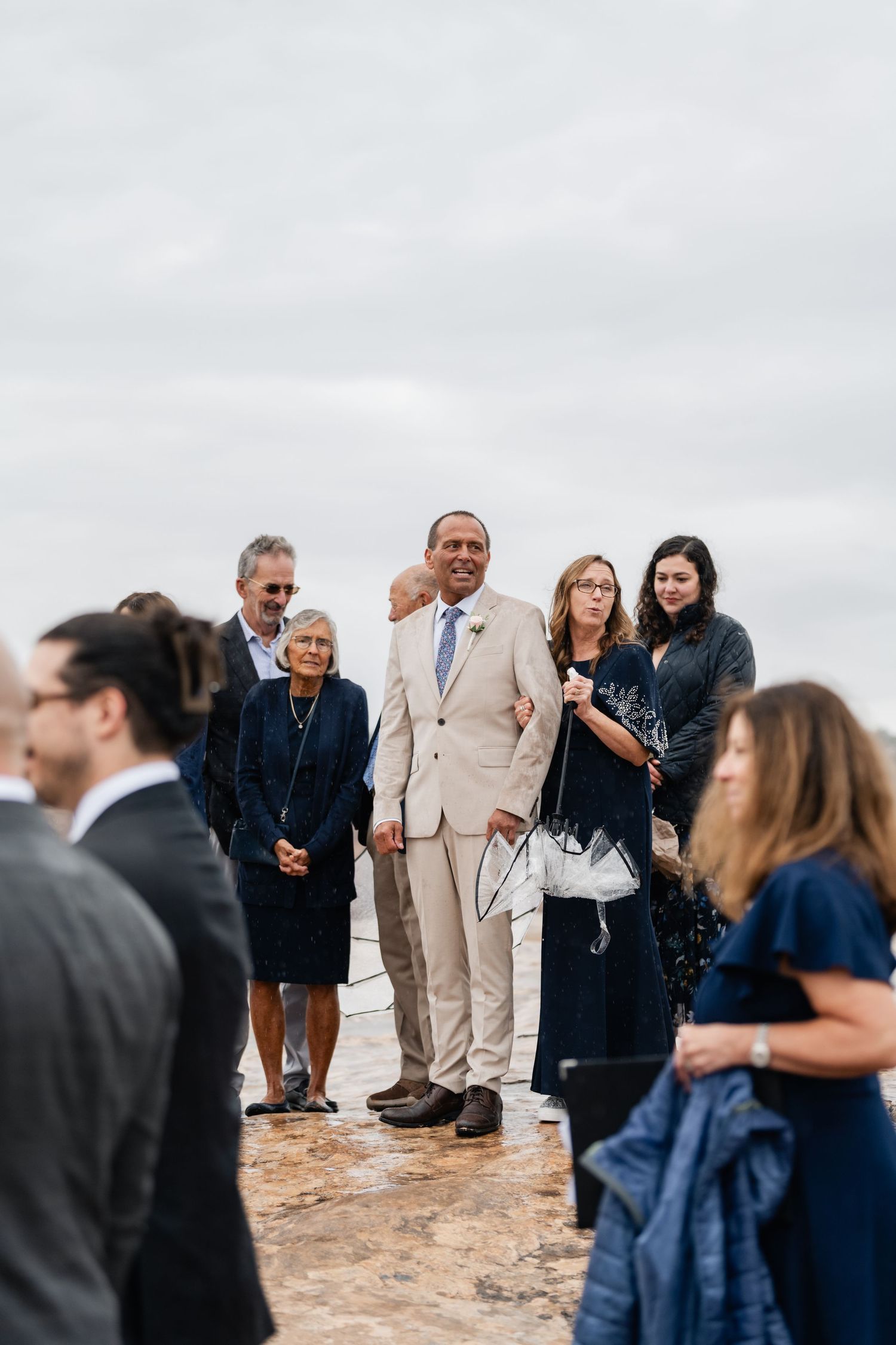 Wedding guests gather on rocky outcrop during outdoor ceremony.