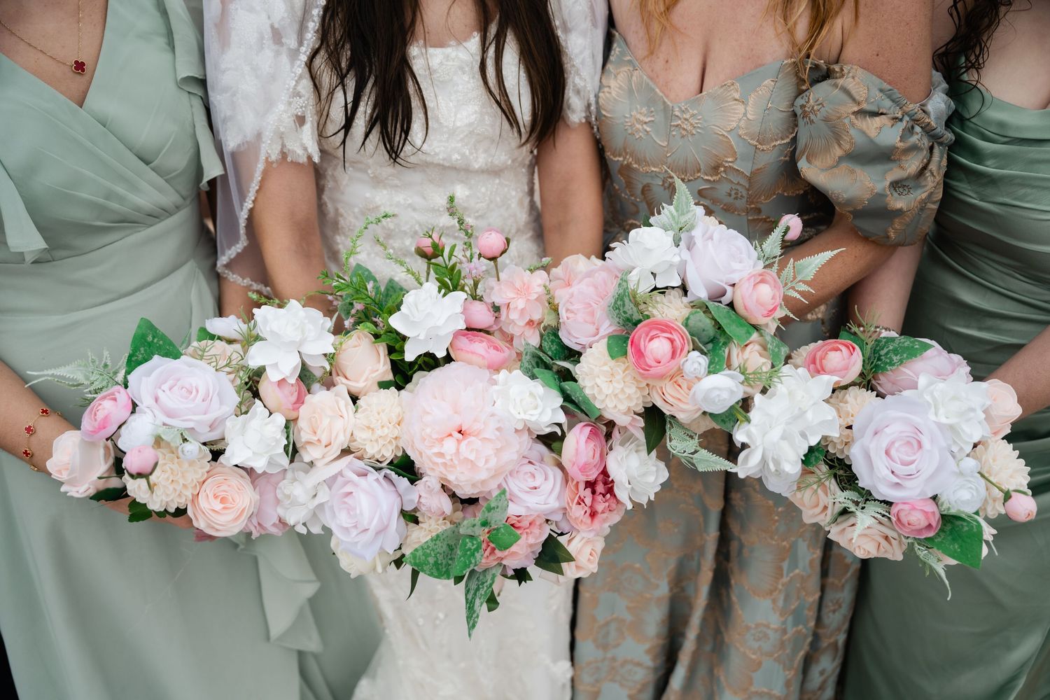 Close-up of pink and white wedding bouquets held by bridesmaids in sage green dresses.