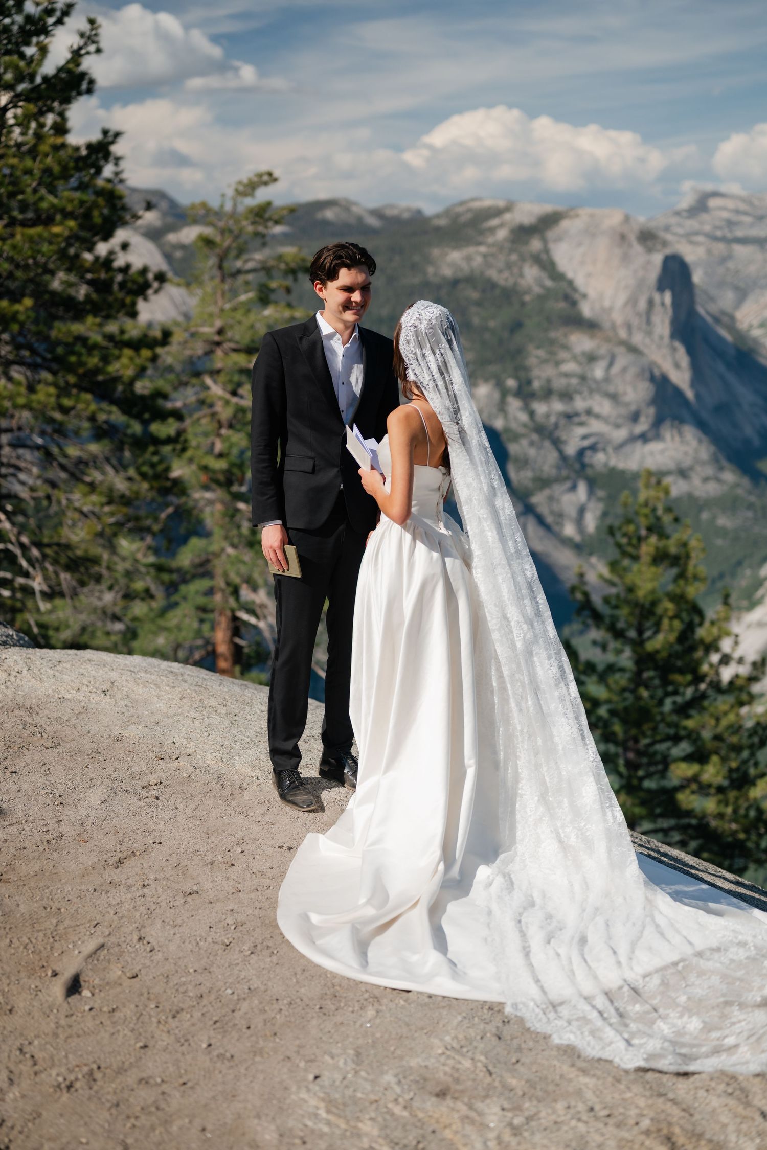 Bride and groom exchange vows on a rocky cliff with stunning Yosemite valley and Half Dome views behind them.