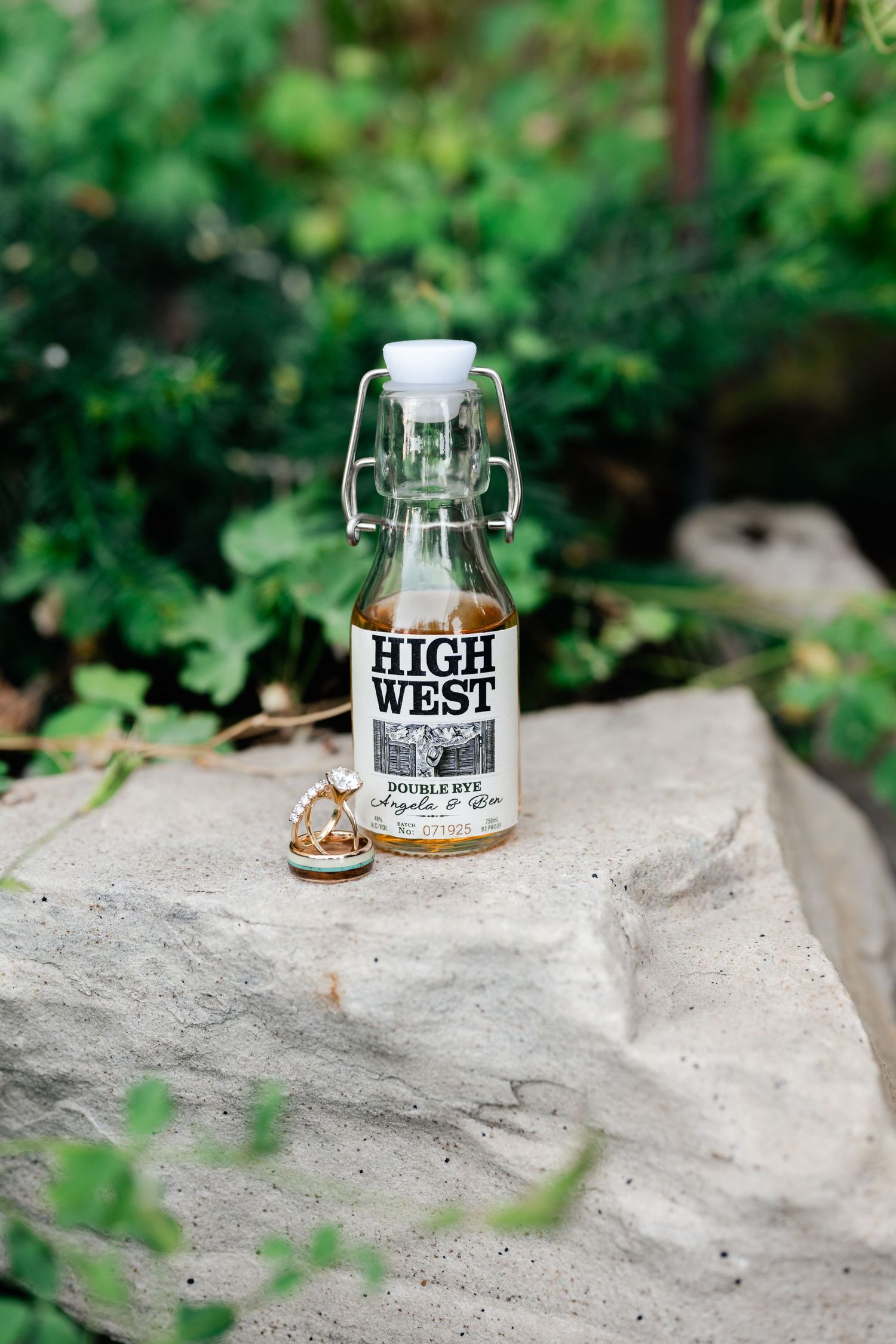 High West Double Rye whiskey bottle with custom label on a stone, surrounded by lush greenery outdoors.