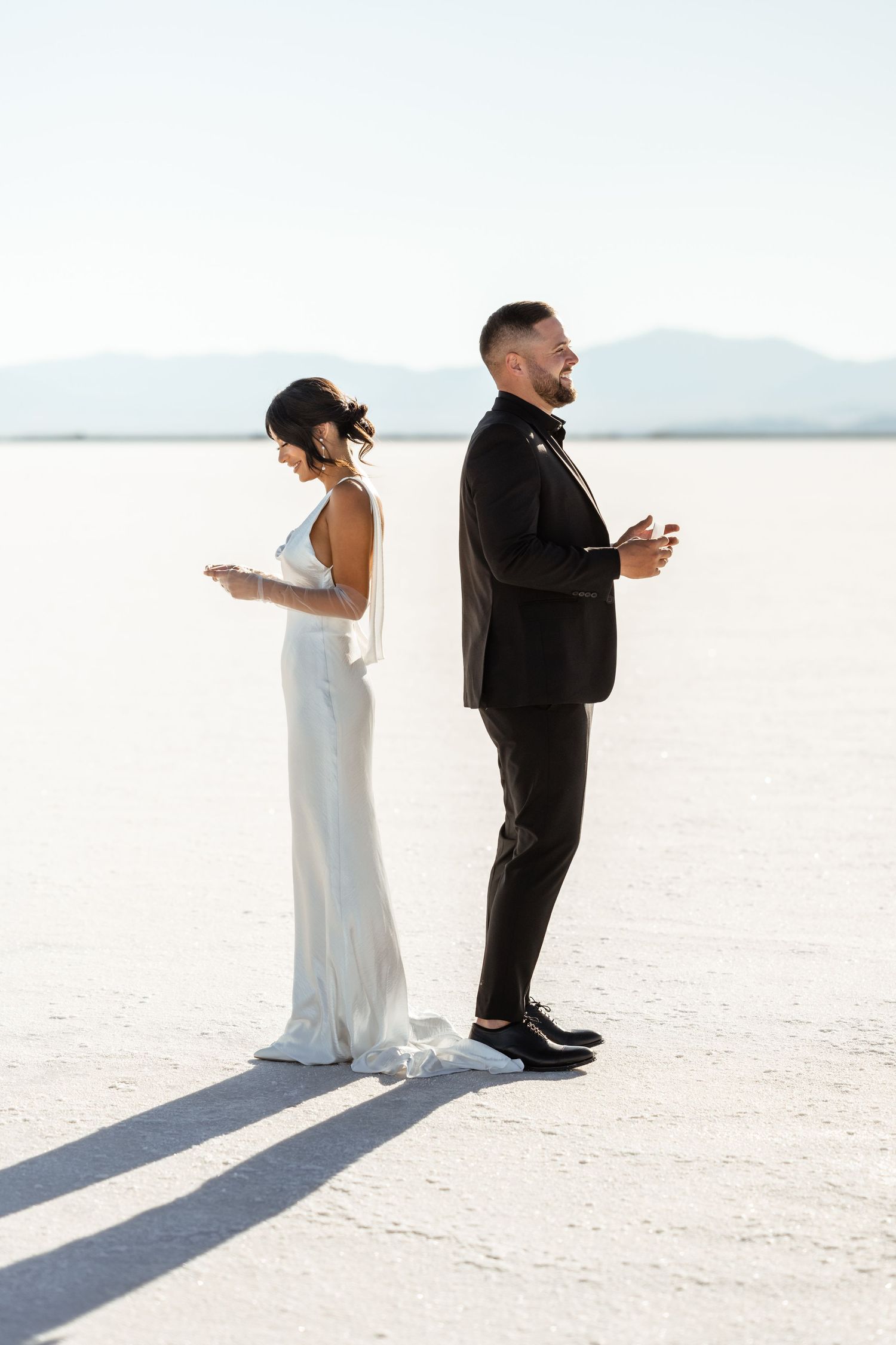 Wedding couple standing on white salt flats casting long shadows in dramatic lighting.