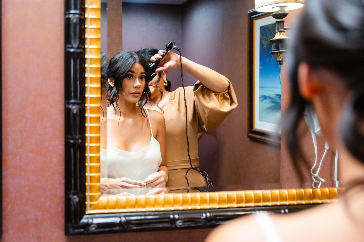 Person styling their hair while looking in a gold-framed mirror mounted on a brown wall.