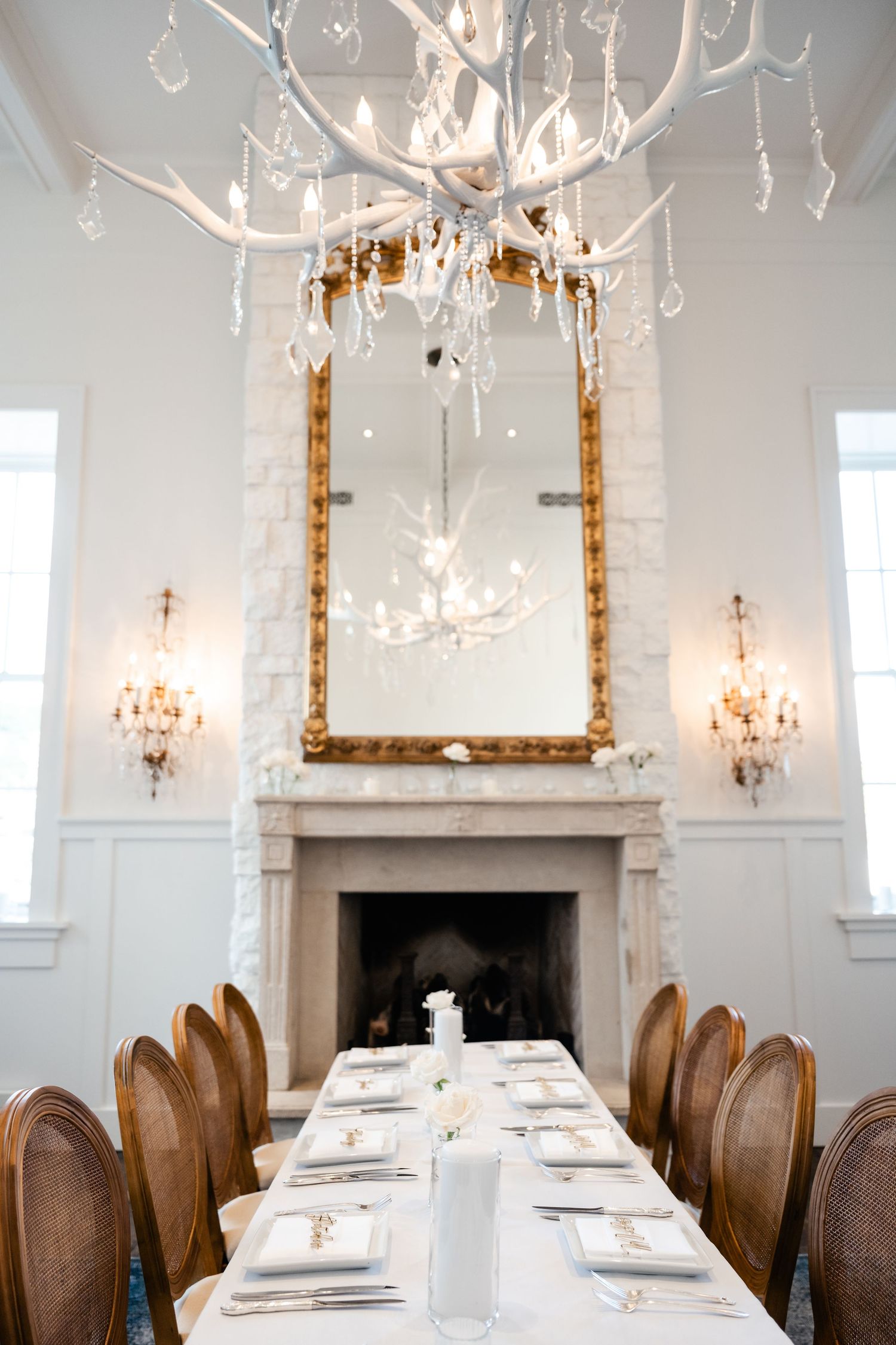 Elegant dining room with crystal chandeliers and wooden chairs set for formal dinner reception.