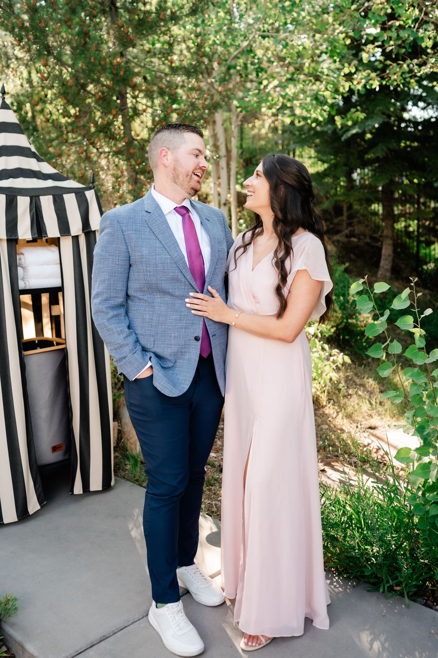 Couple shares a joyful moment outdoors against a backdrop of greenery and black and white decor.