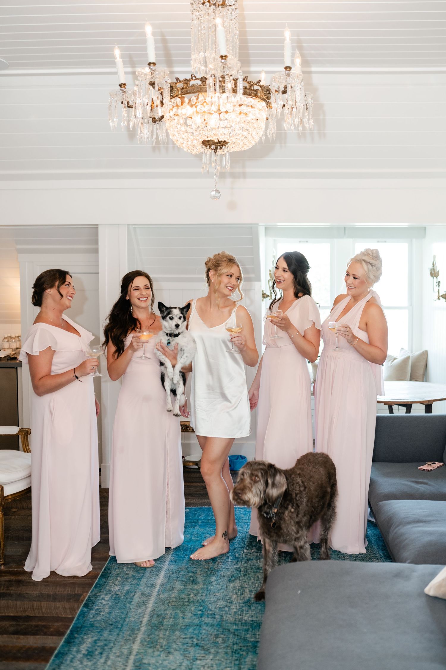 Group wearing matching pink robes gathered in elegant room with crystal chandelier and blue carpet.