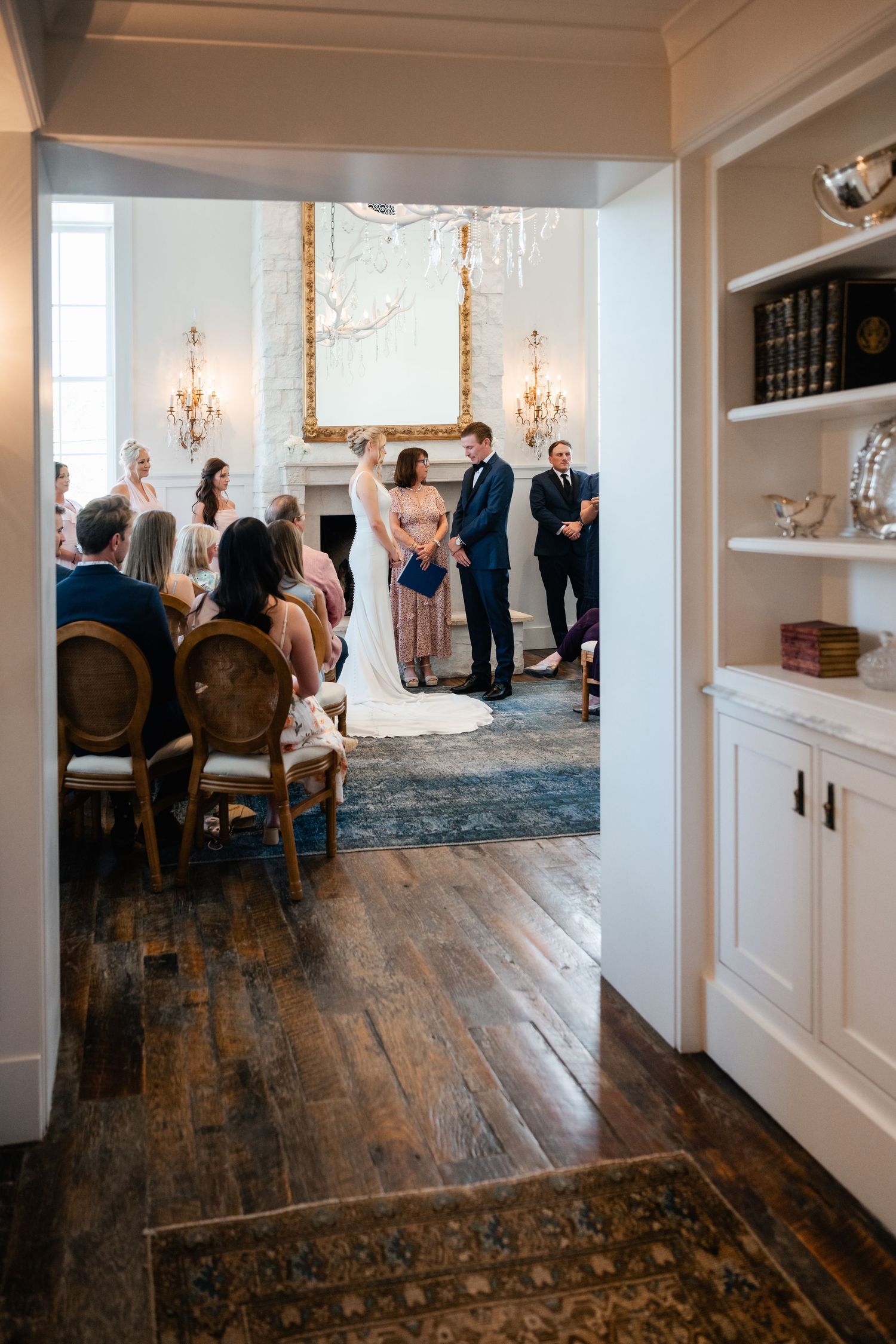 Interior view of a wedding venue with hardwood floors, white wainscoting, and chandeliers.