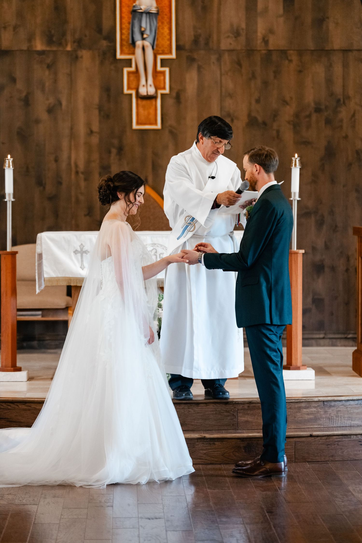 A wedding ceremony takes place in a rustic chapel with wooden walls and white decorative elements.