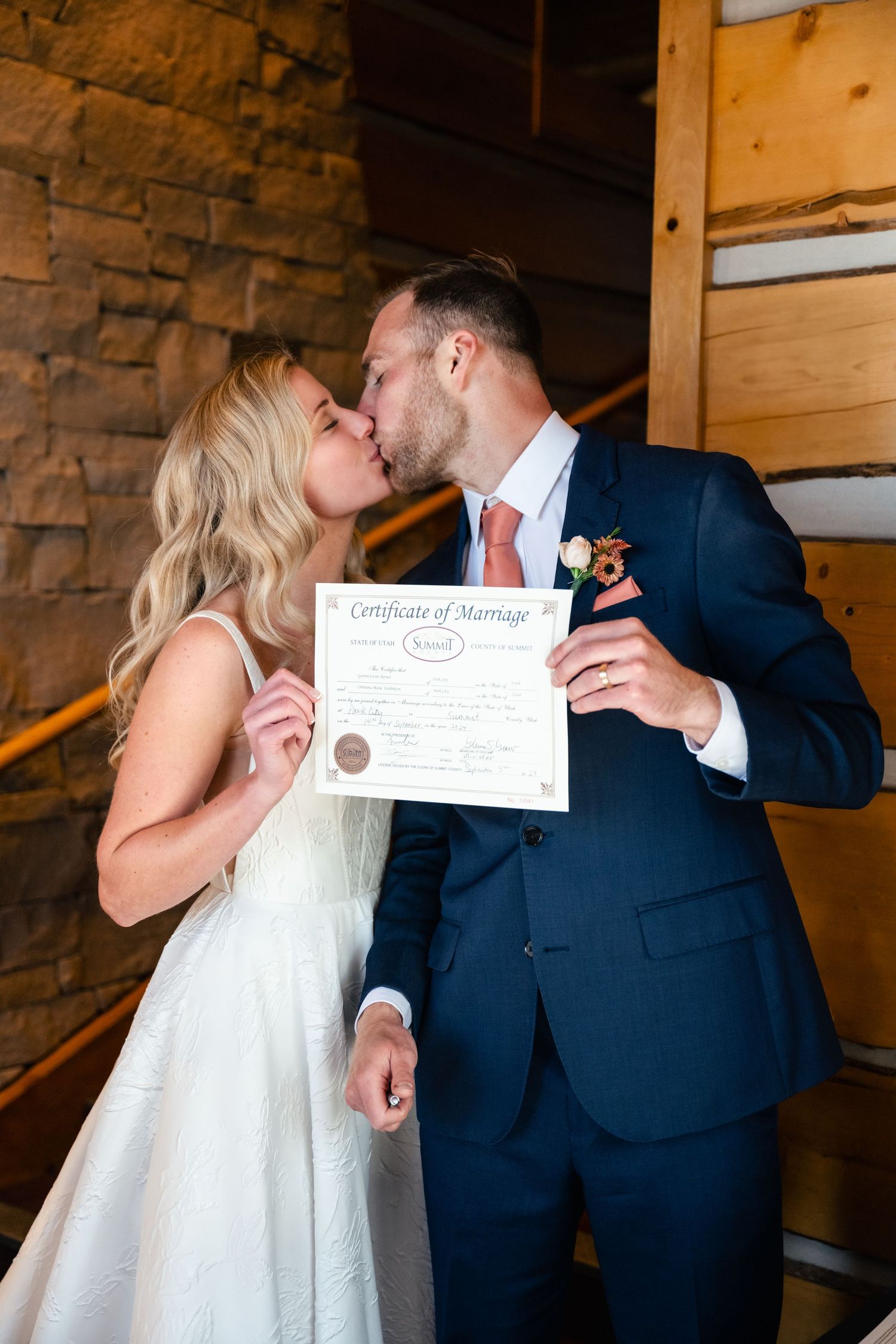 Couple shares intimate moments while holding their marriage certificate in a rustic venue.