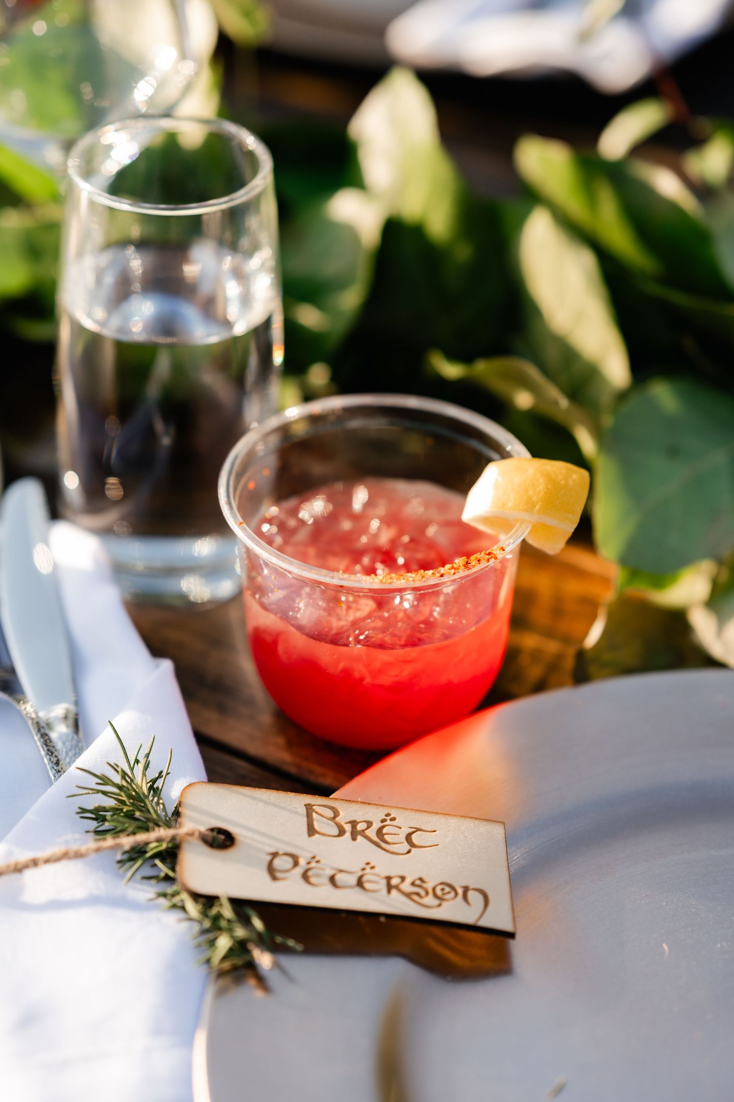 Red cocktails garnished with citrus and rosemary sit beside place cards at a wedding reception.
