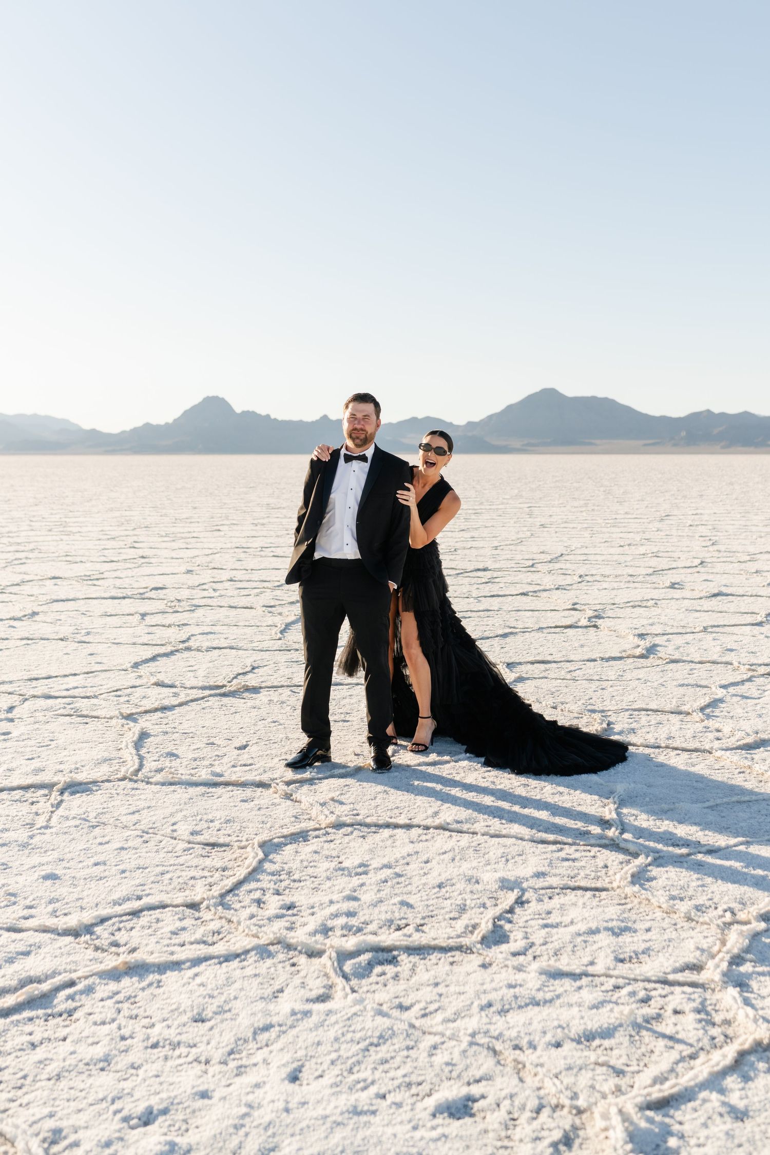 A couple being silly on the stark white salt flats during a formal photo session at sunset. Utah Salt Flats Photographer.