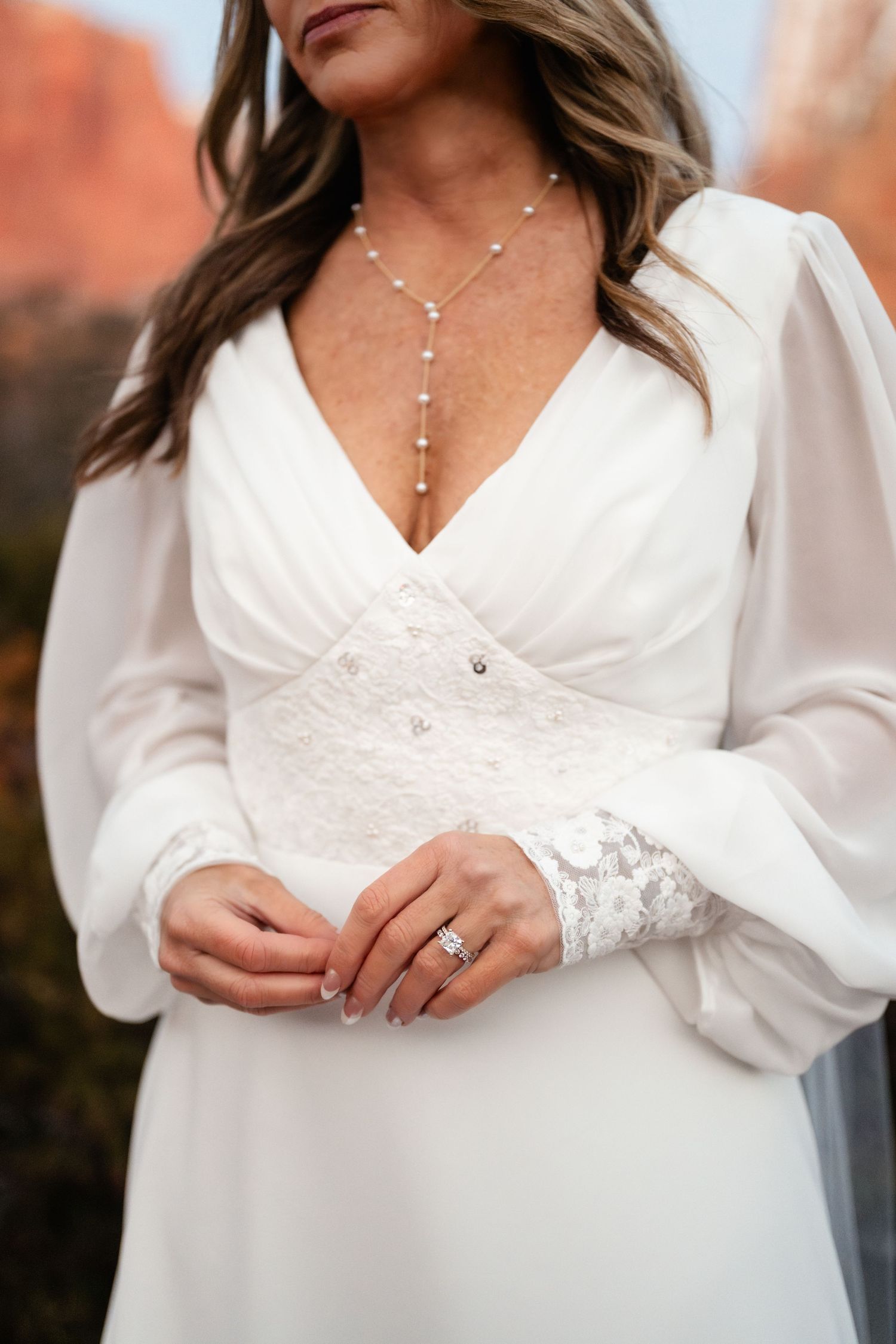 Close-up details of a white wedding dress with lace sleeves and delicate jewelry.