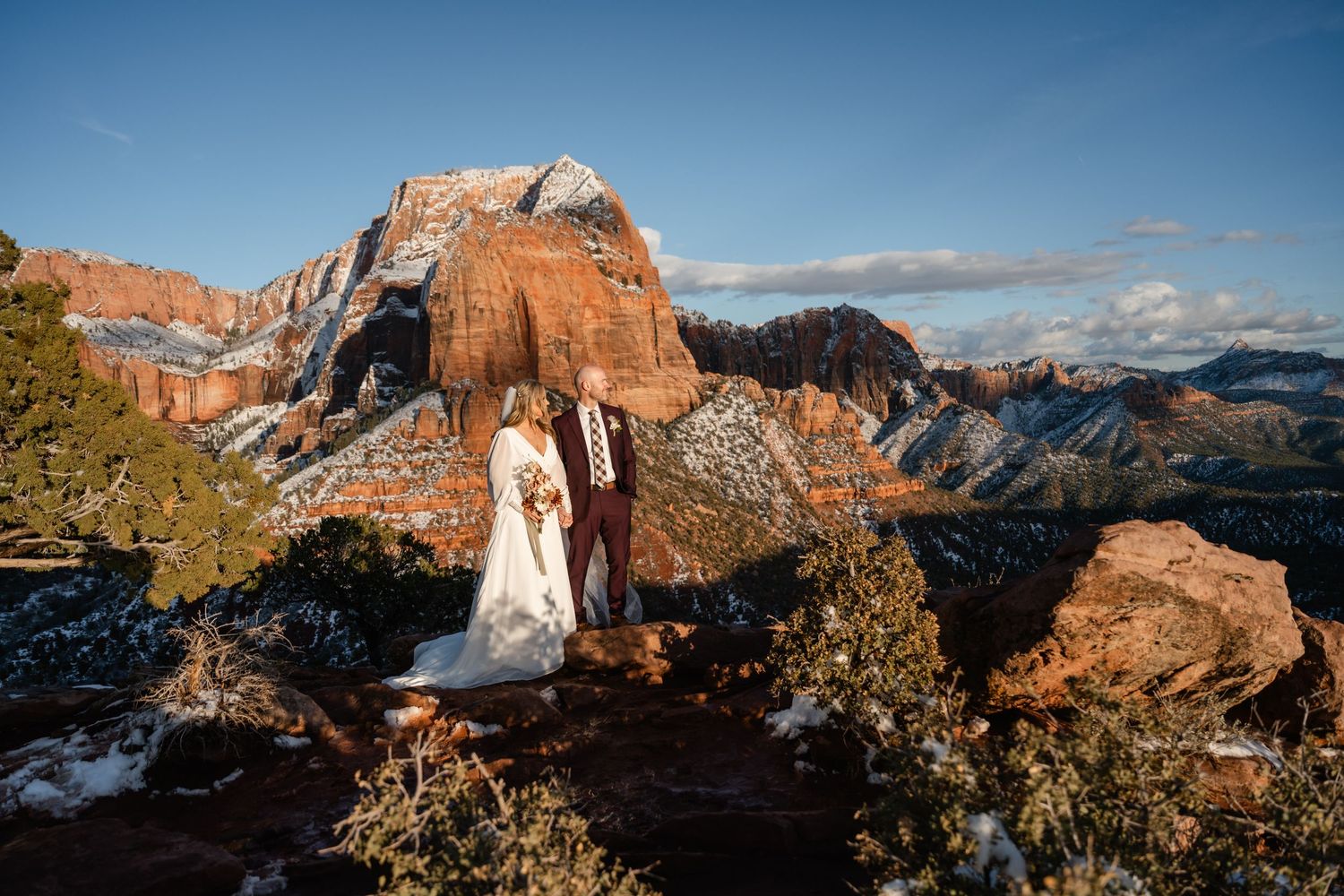 Panoramic view of snow-covered red rock formations in Arches National Park against a blue winter sky.