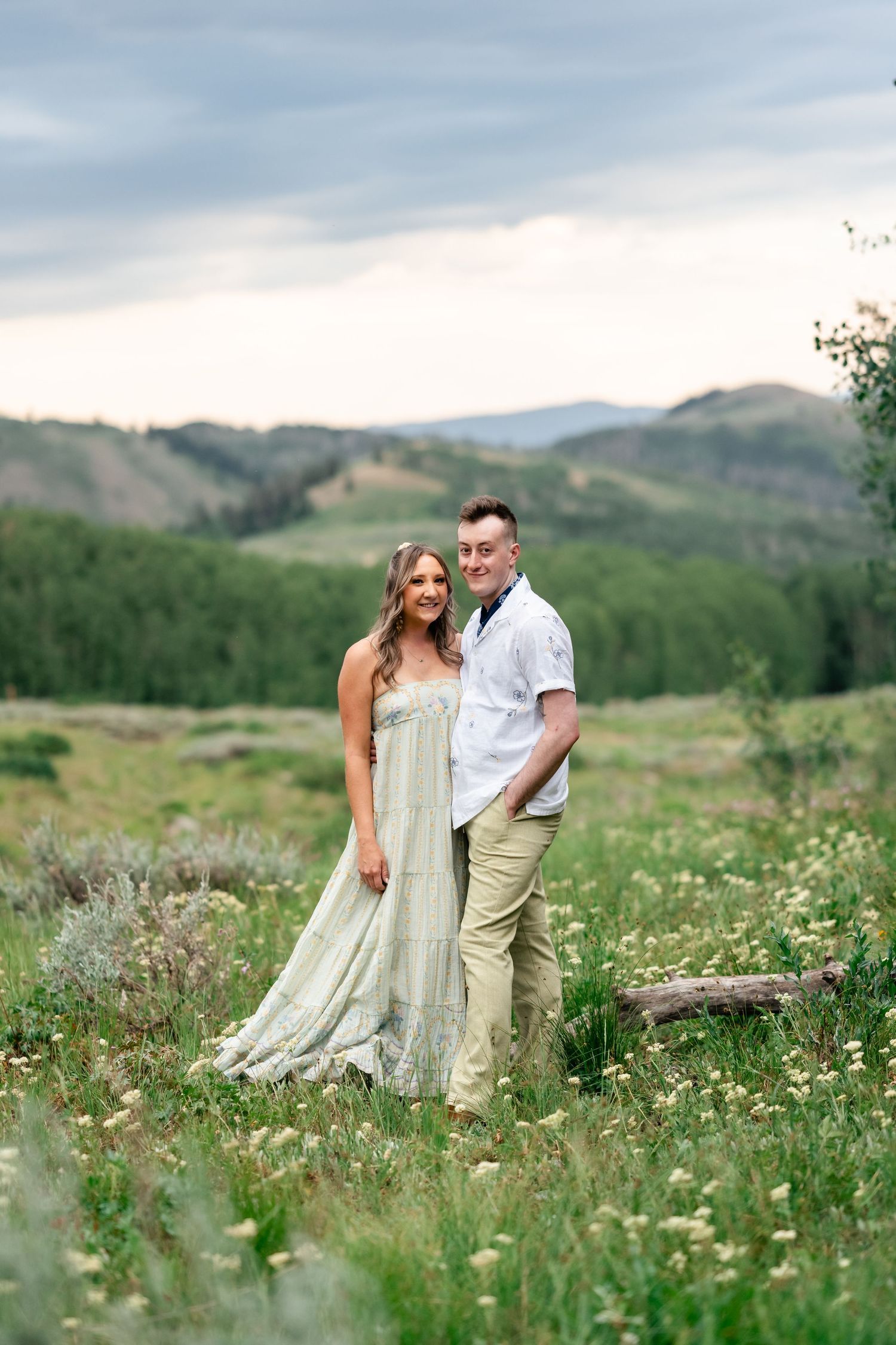 A romantic photoshoot in a mountain meadow filled with white wildflowers and green grass.