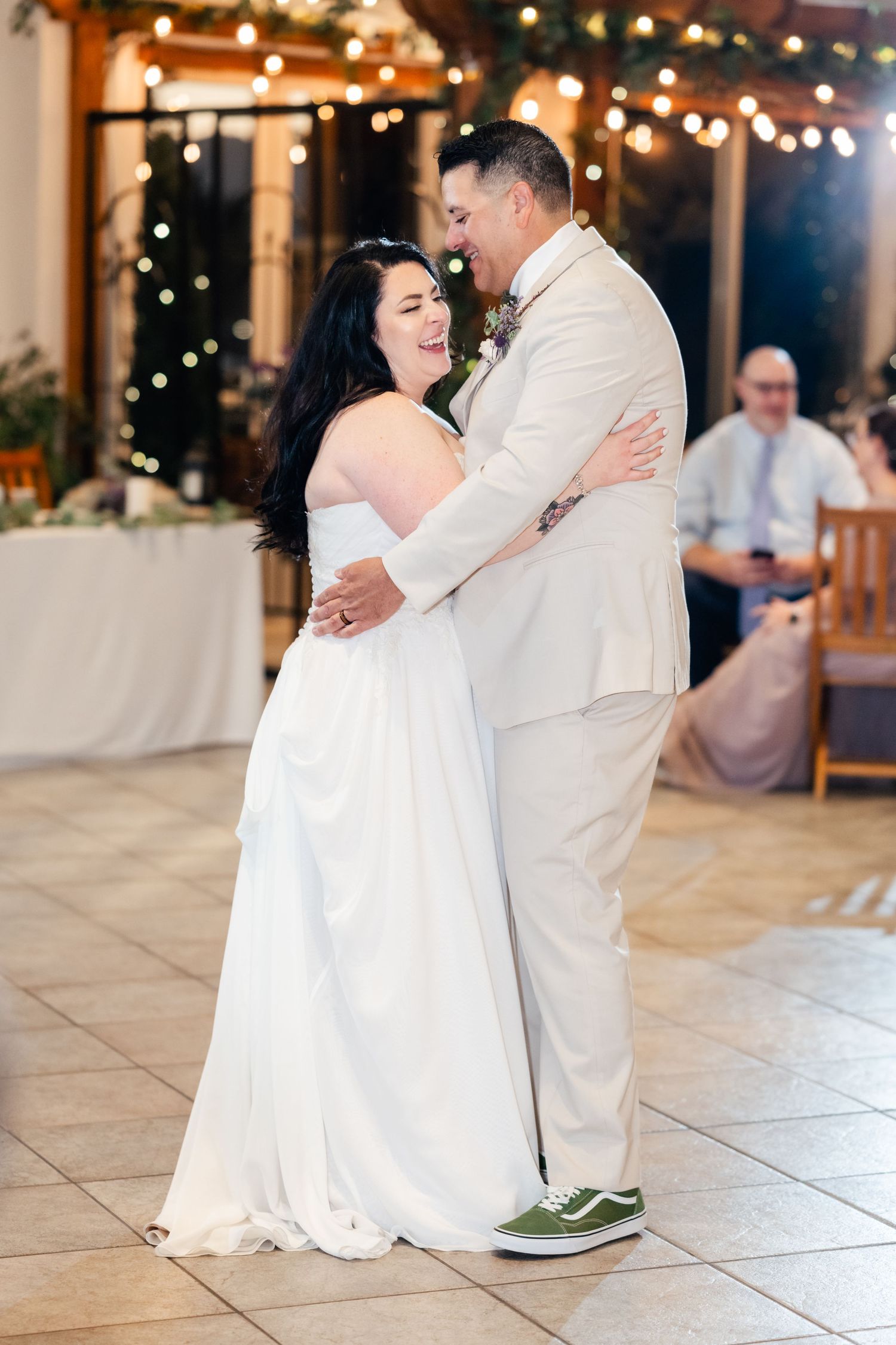 A couple shares their first dance together at a wedding reception with twinkle lights in background.