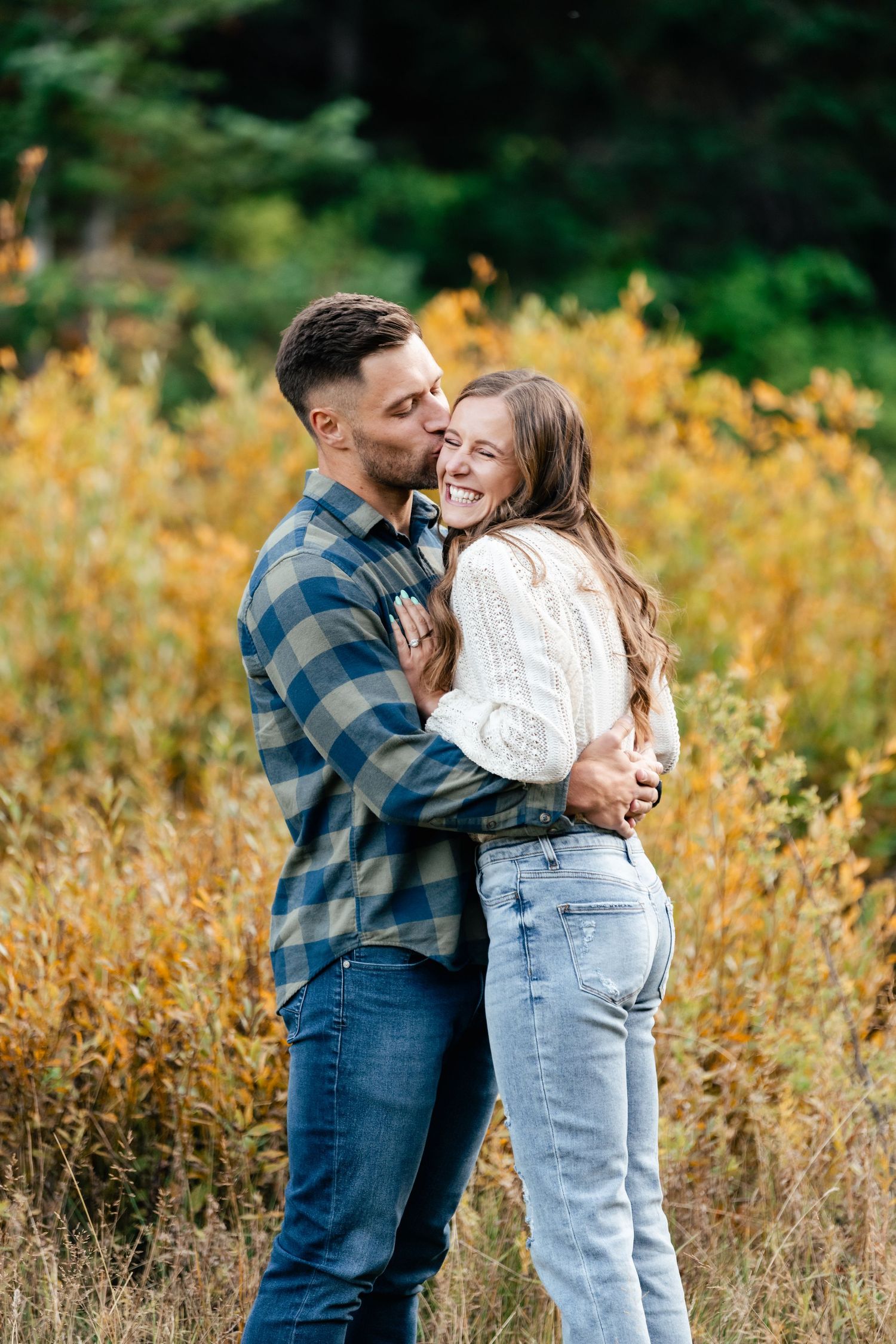 A couple shares a joyful embrace while laughing together in a field of golden autumn grass.