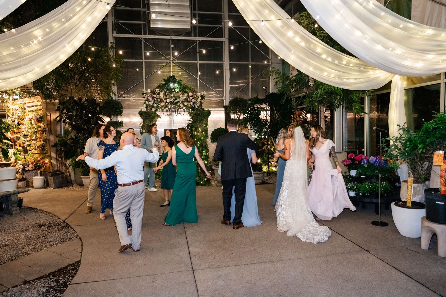 Stylish wedding reception outdoors at dusk with string lights, floral decor and guests dancing on patio.