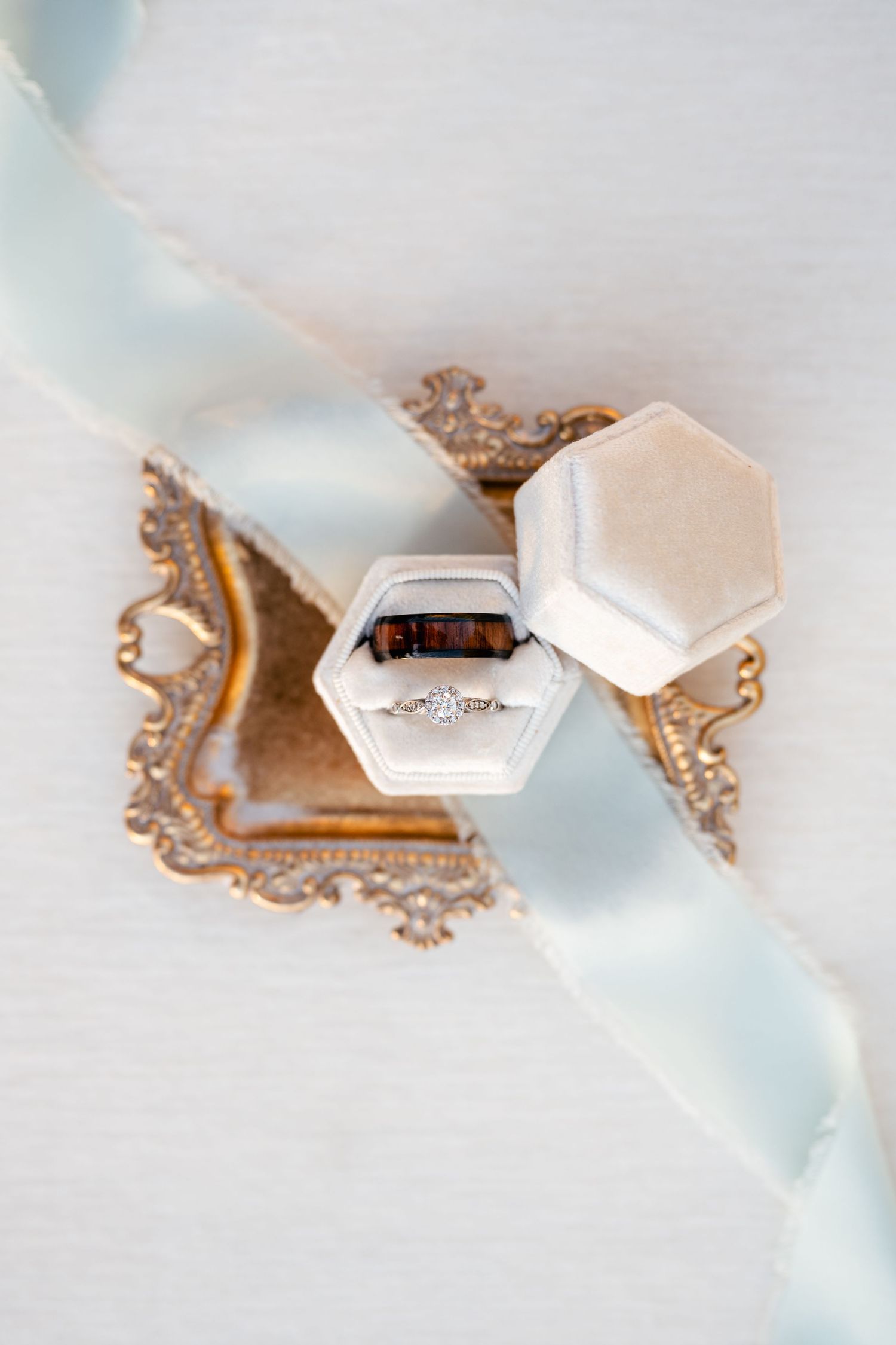 Diamond engagement ring displayed in a white hexagonal ring box with vintage gold frame and light blue silk ribbon decor.