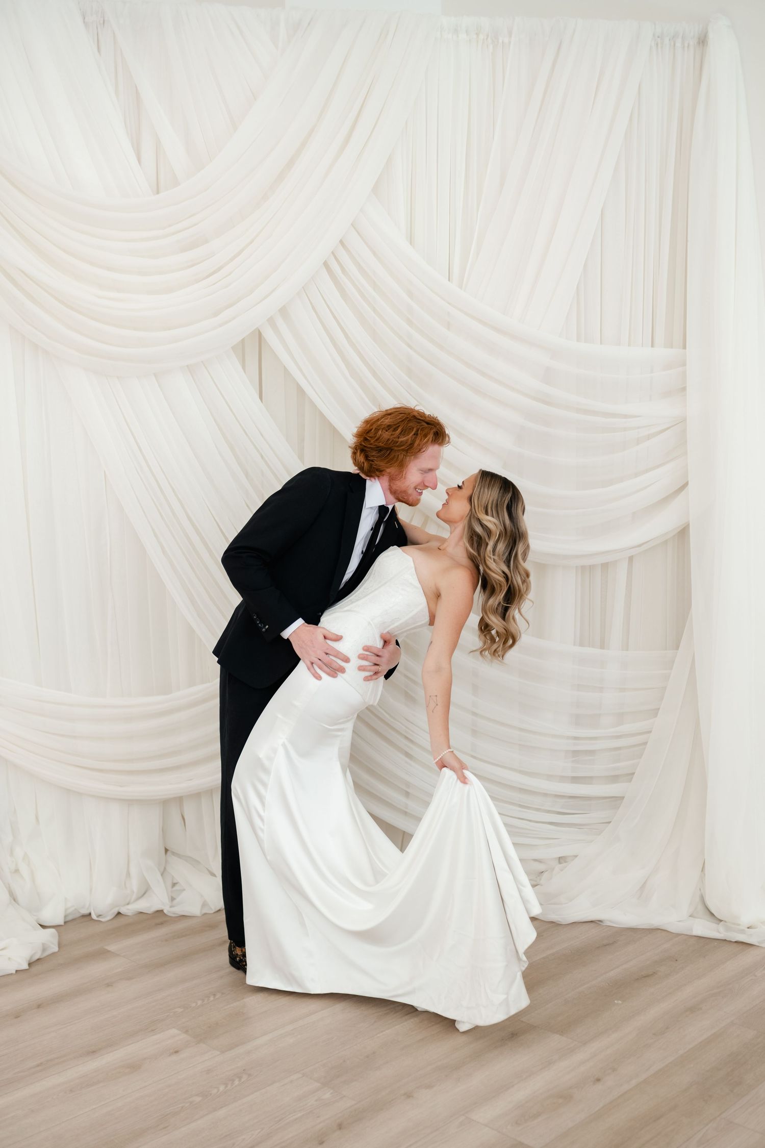 Romantic wedding couple dips by elegant fabric draping in wedding attire at Moments on Main by Utah wedding photographer and videographer.