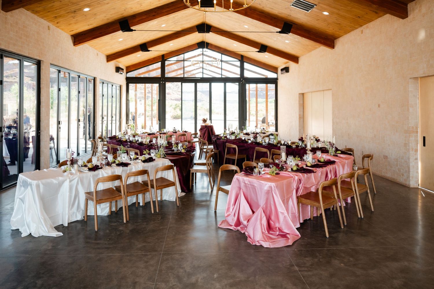 Elegant Moab wedding with vaulted wood ceiling, long tables with pink and white linens, floral centerpieces, and large windows.
