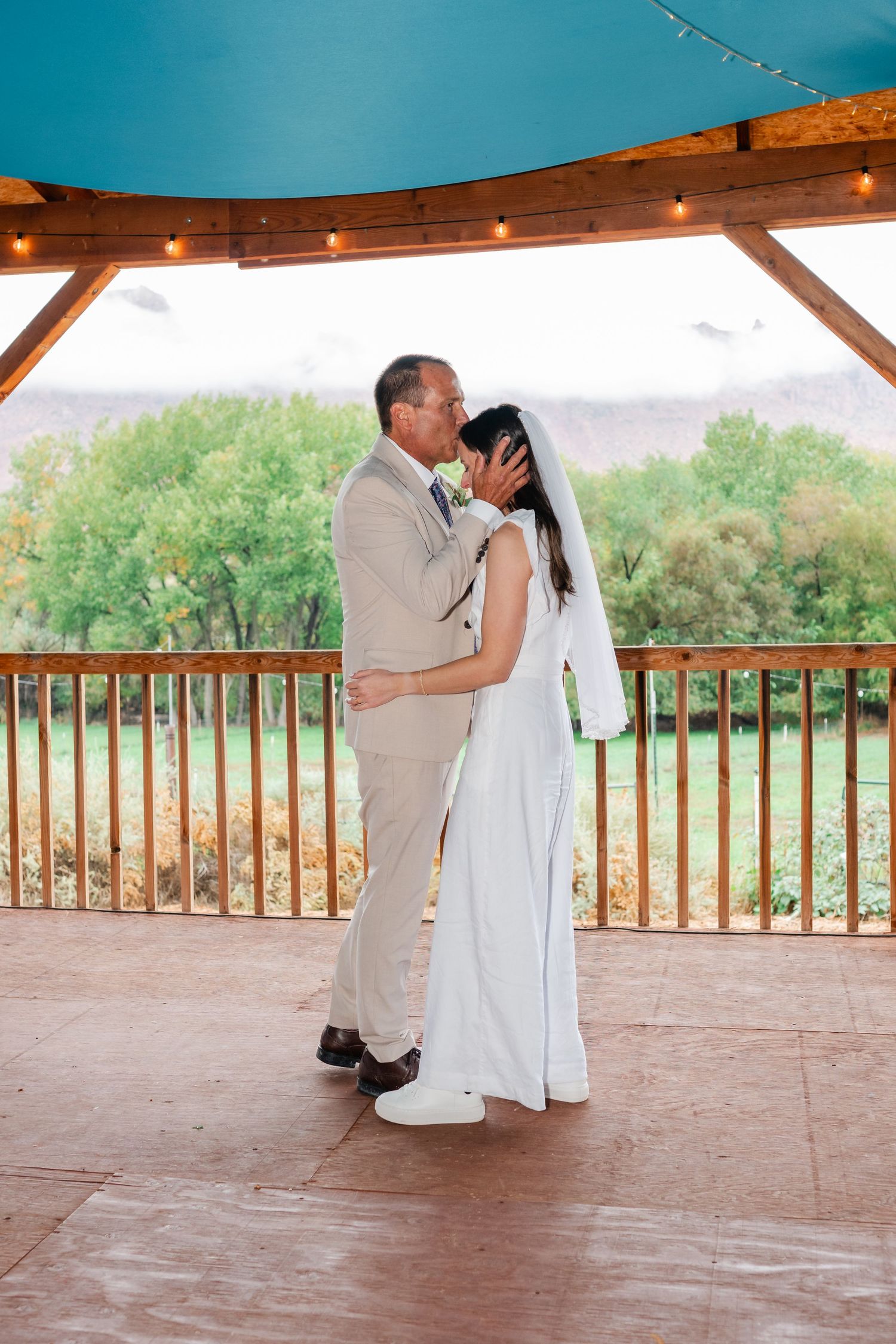 Couple sharing their first kiss as newlyweds on a covered outdoor deck with scenic views.