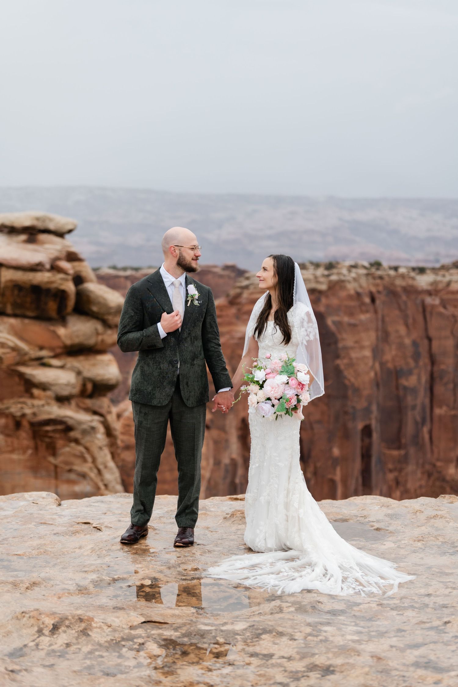 A wedding couple shares a joyful moment on dramatic red rock cliffs during their desert ceremony.