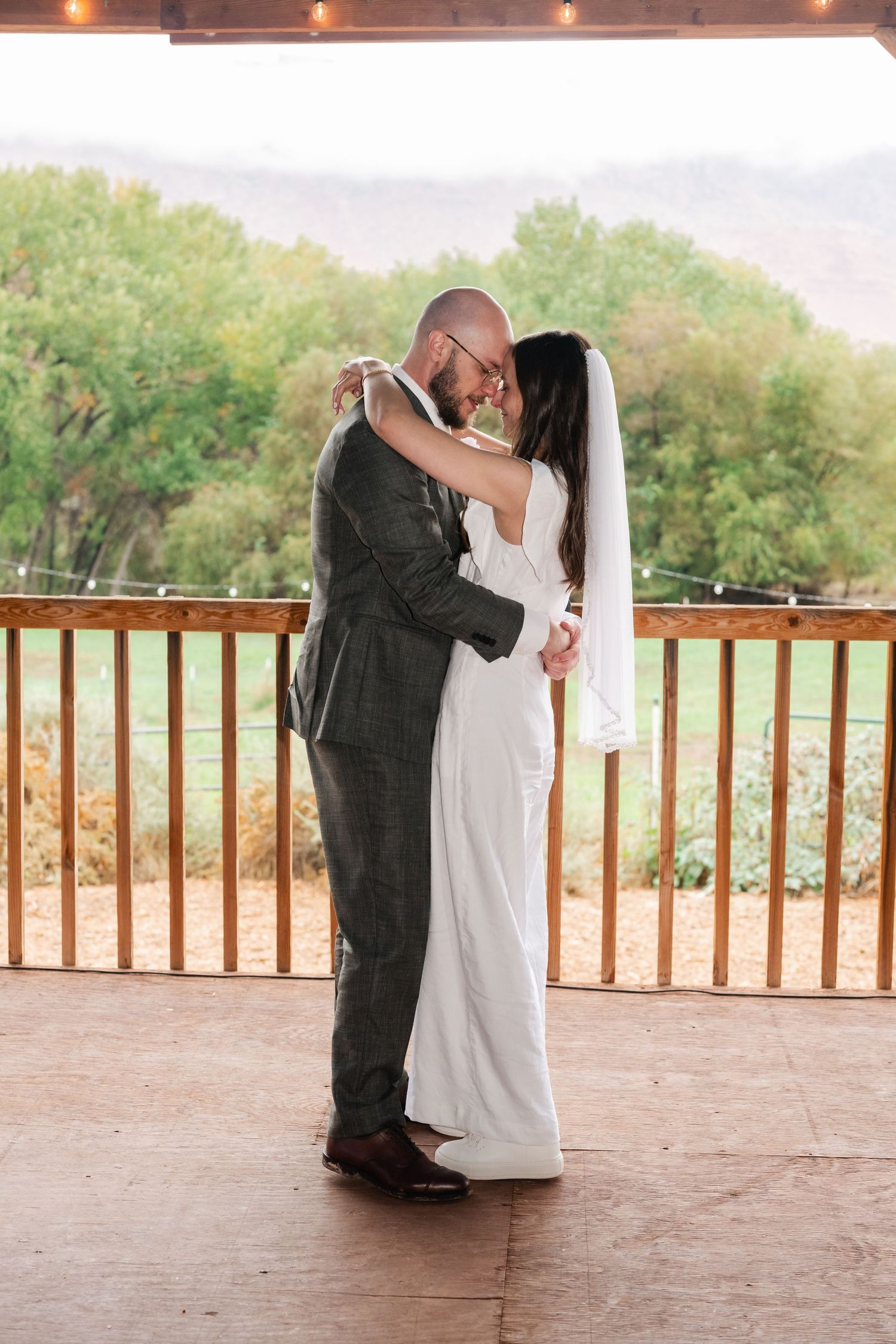 A couple shares a romantic dance on a covered outdoor deck with greenery in background.