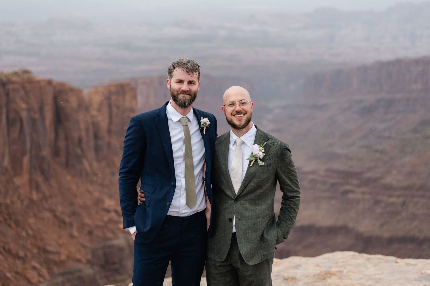 Wedding party members pose together against a dramatic desert canyon backdrop.