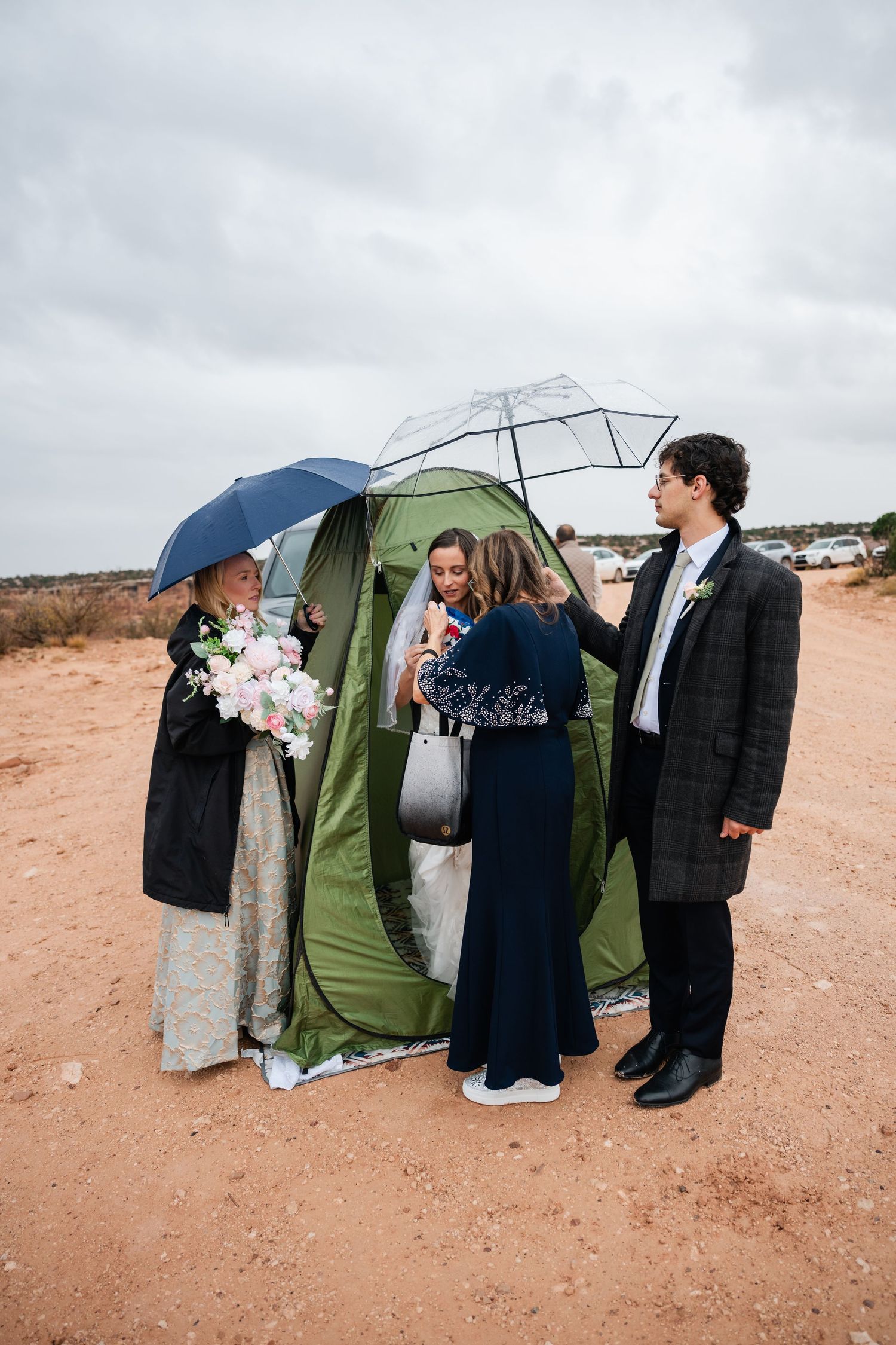 Wedding party gathered under umbrellas on a cloudy day in a desert landscape.