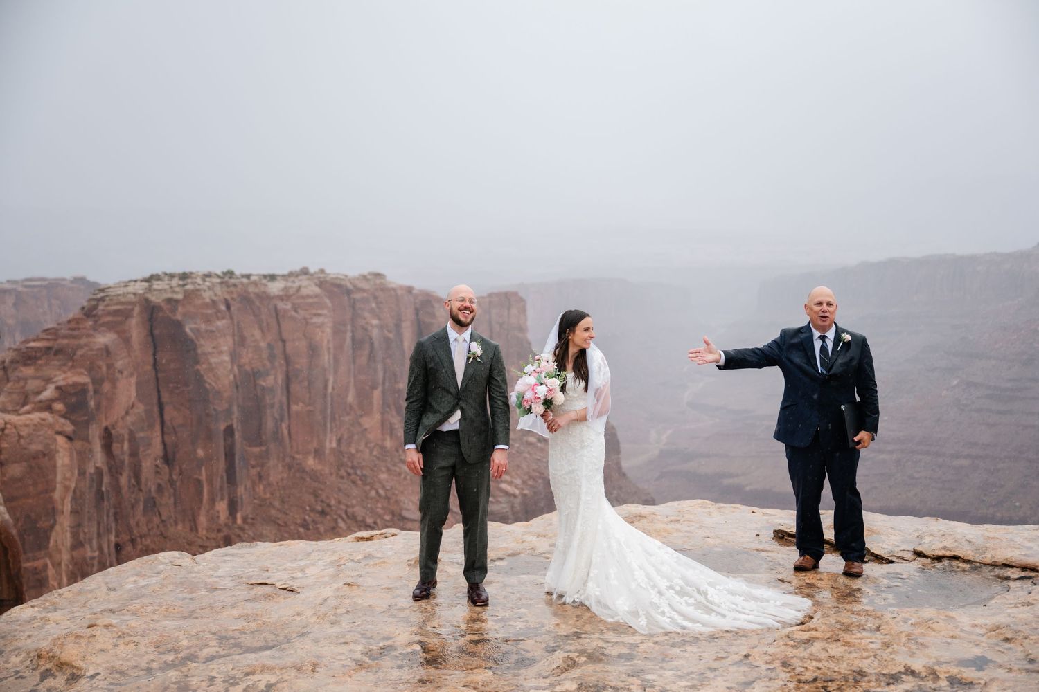 Wedding ceremony taking place on dramatic cliffside overlook with vast canyon views in background.