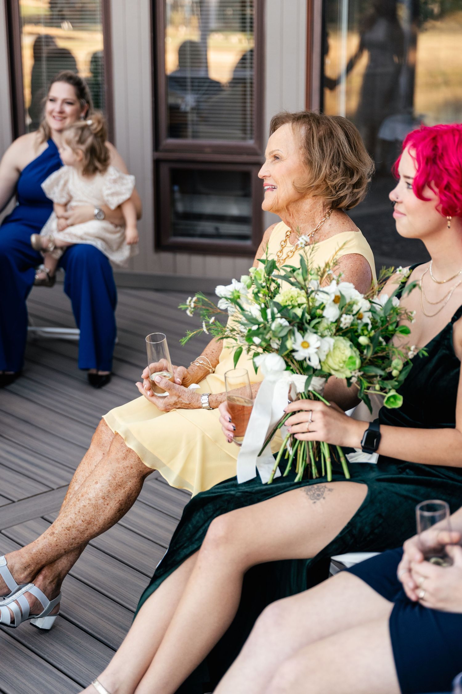 Wedding guests seated on a deck holding bouquets and enjoying the ceremony.