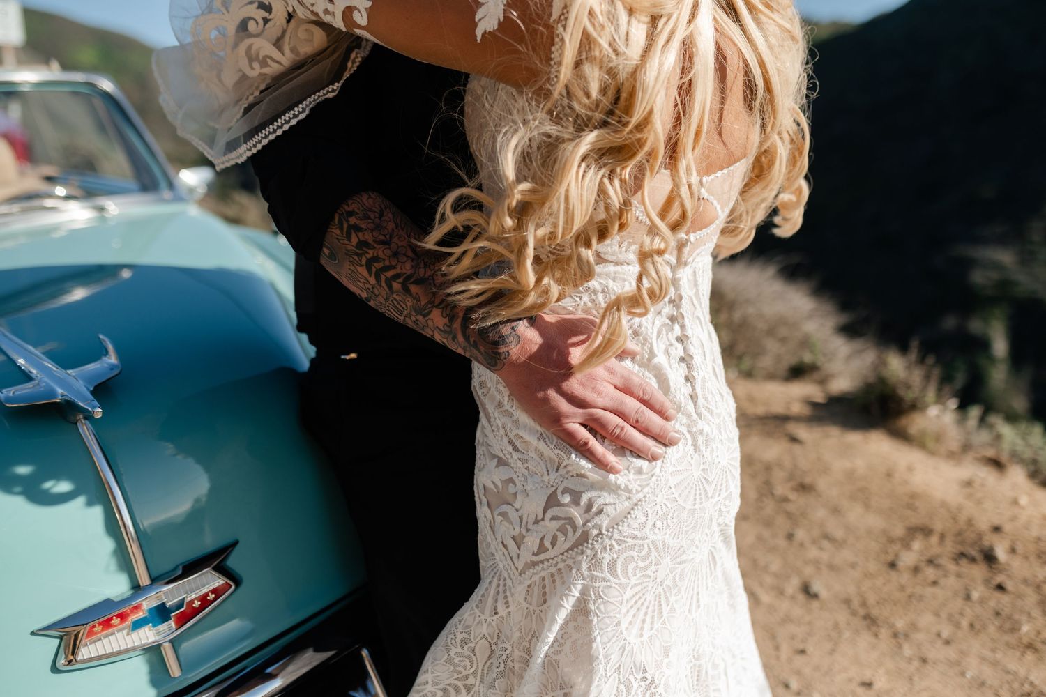 Close-up detail of a lace wedding dress against a vintage turquoise car.